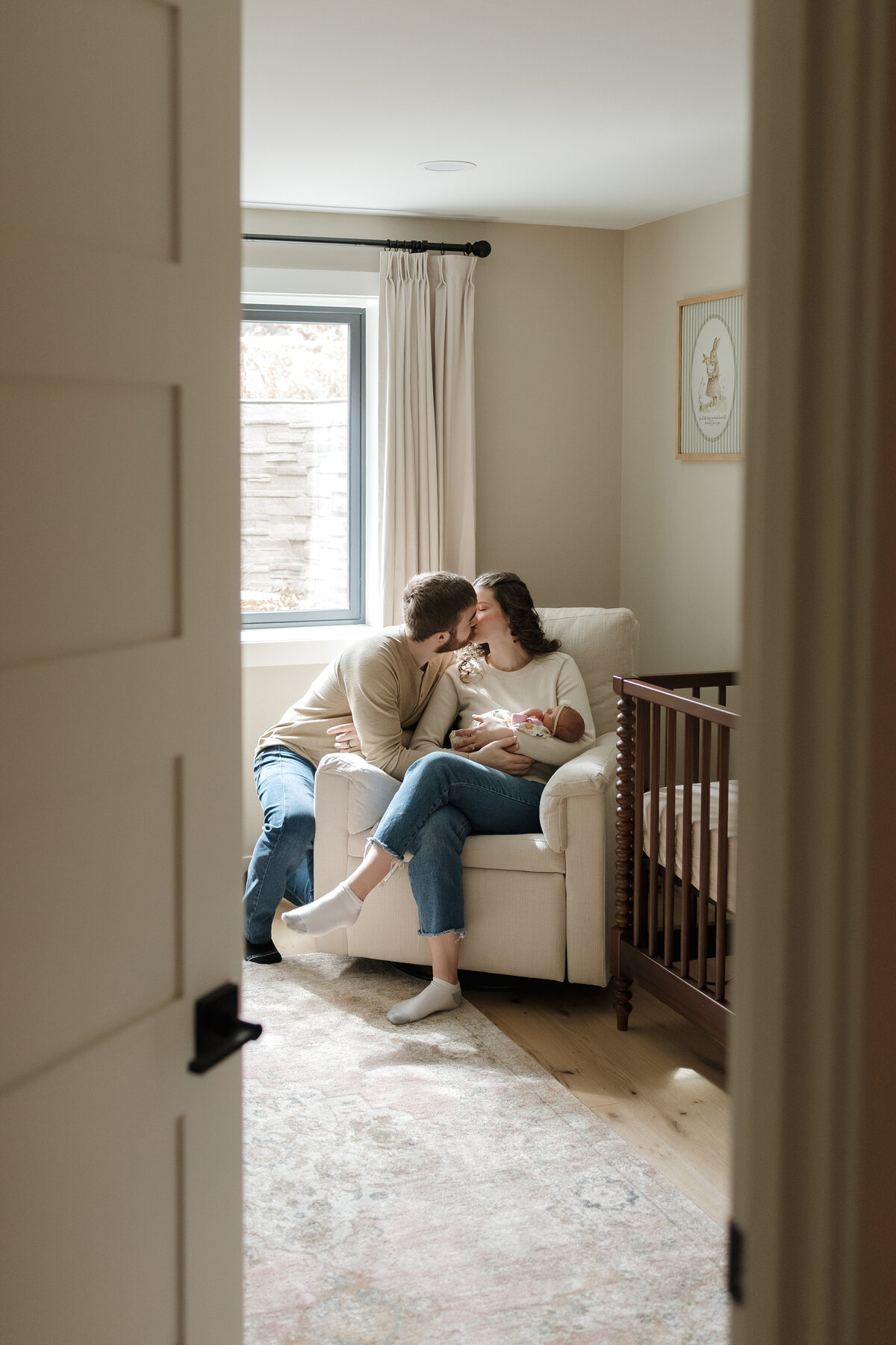 Longmont new mom and dad kissing while holding newborn baby in rocking chair