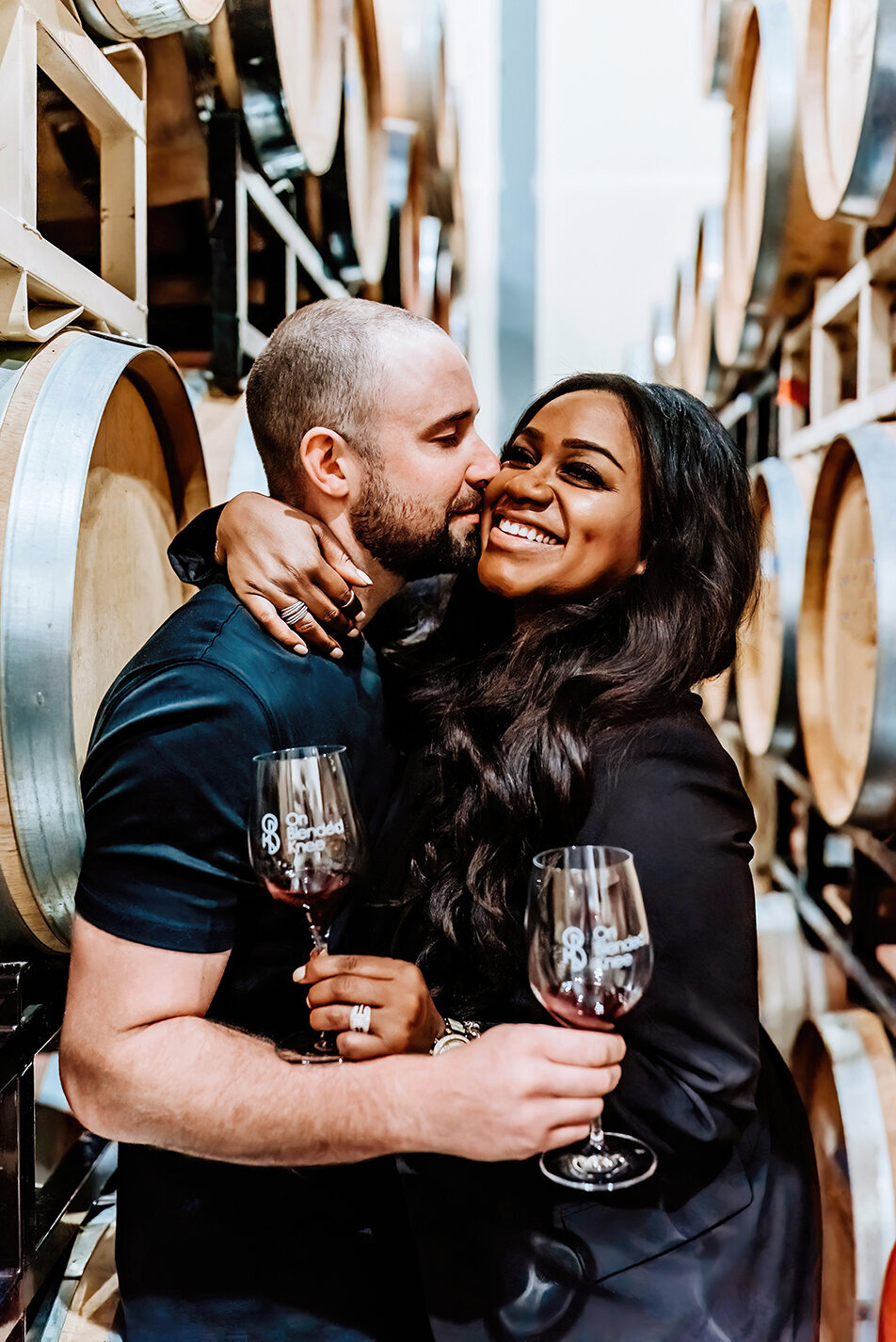 a headshot session for a boutique winery owners, husband and wife holding wine glasses embracing in a hug smiling