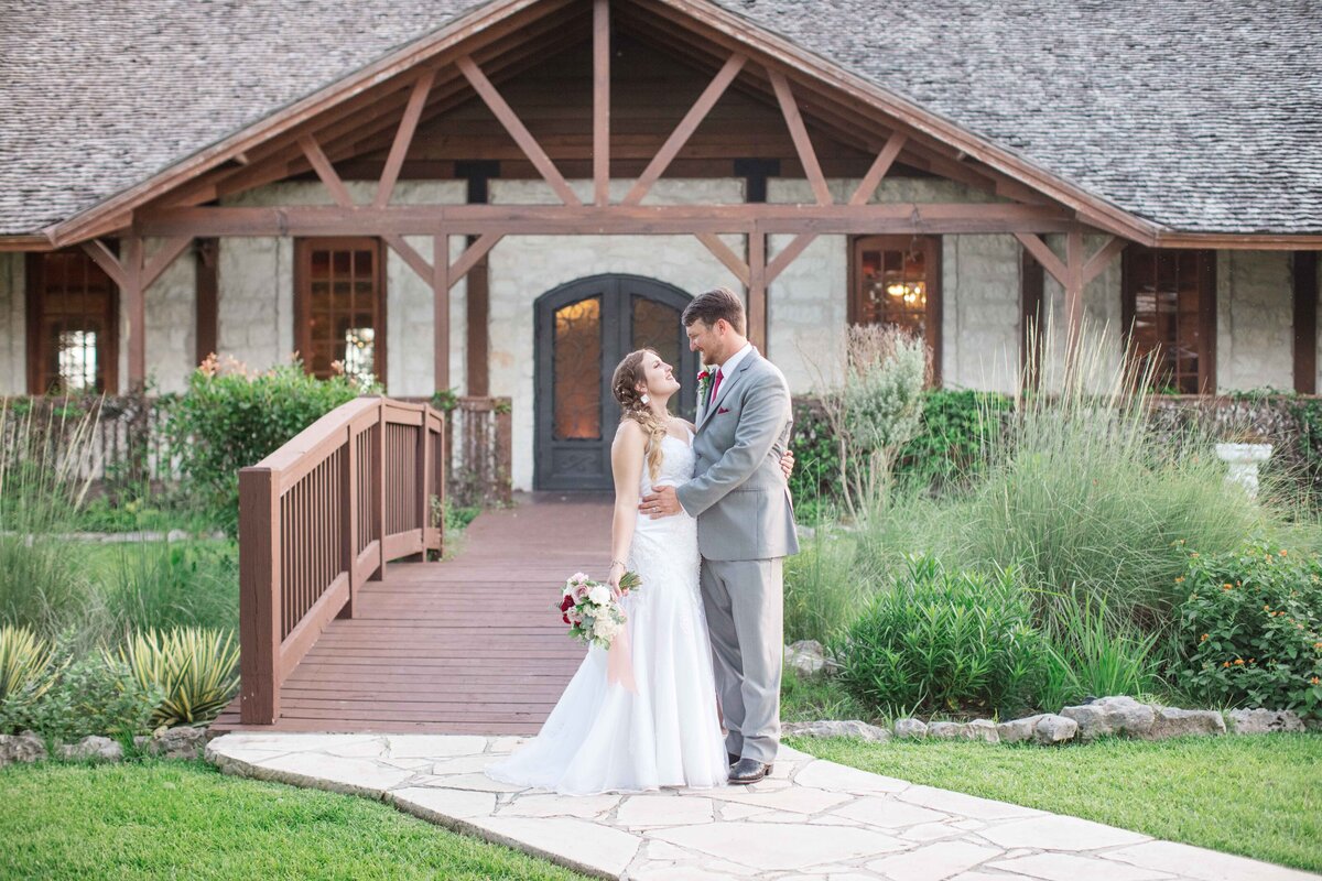 bride and groom embrace in front of wooden bridge at Milestone New Braunfels wedding