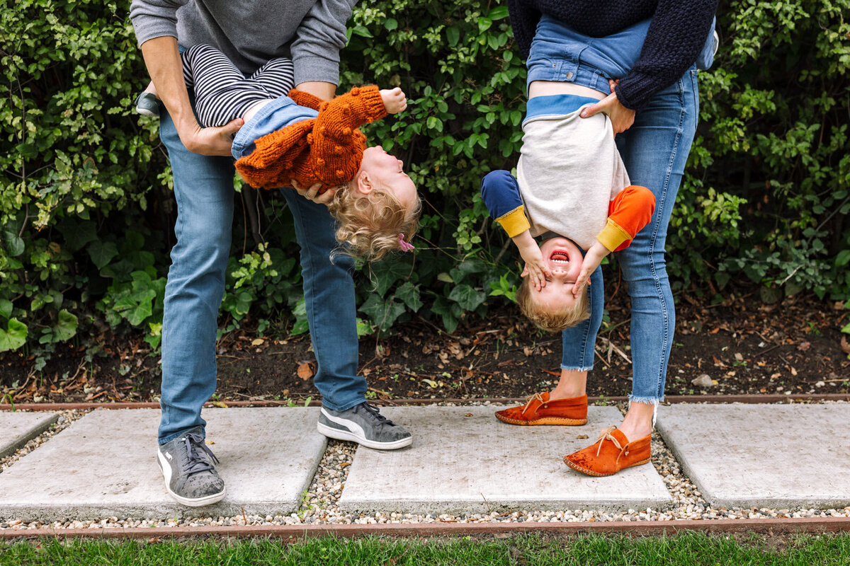mom and dad holding their two young kids upside down in Oakland backyard as kids laugh