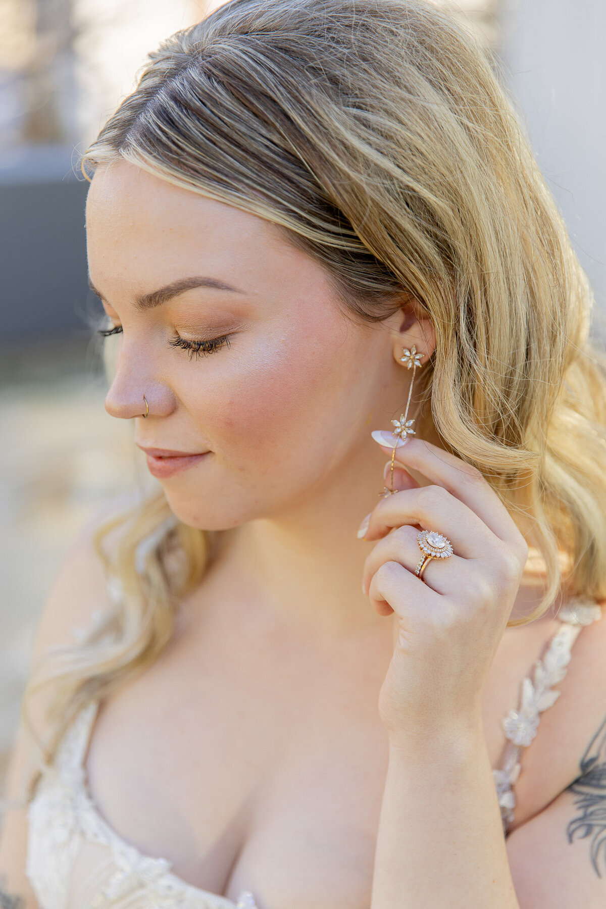 Touching her earring with one hand, a bride looks down at the ground for a posed picture.