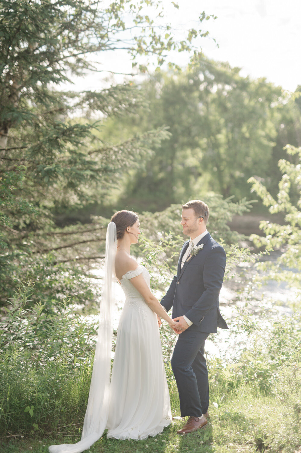 Les amoureux savourent un moment discret et complice au bord de la rivière Rouge dans les Laurentides, scène intime et naturelle d’un mariage au charme paisible