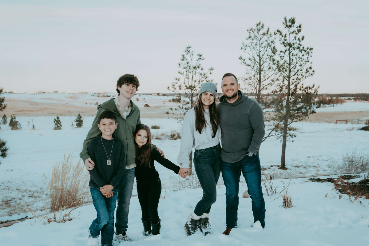 A family of five stands on their property, holding hands and posing for a family Christmas card photo