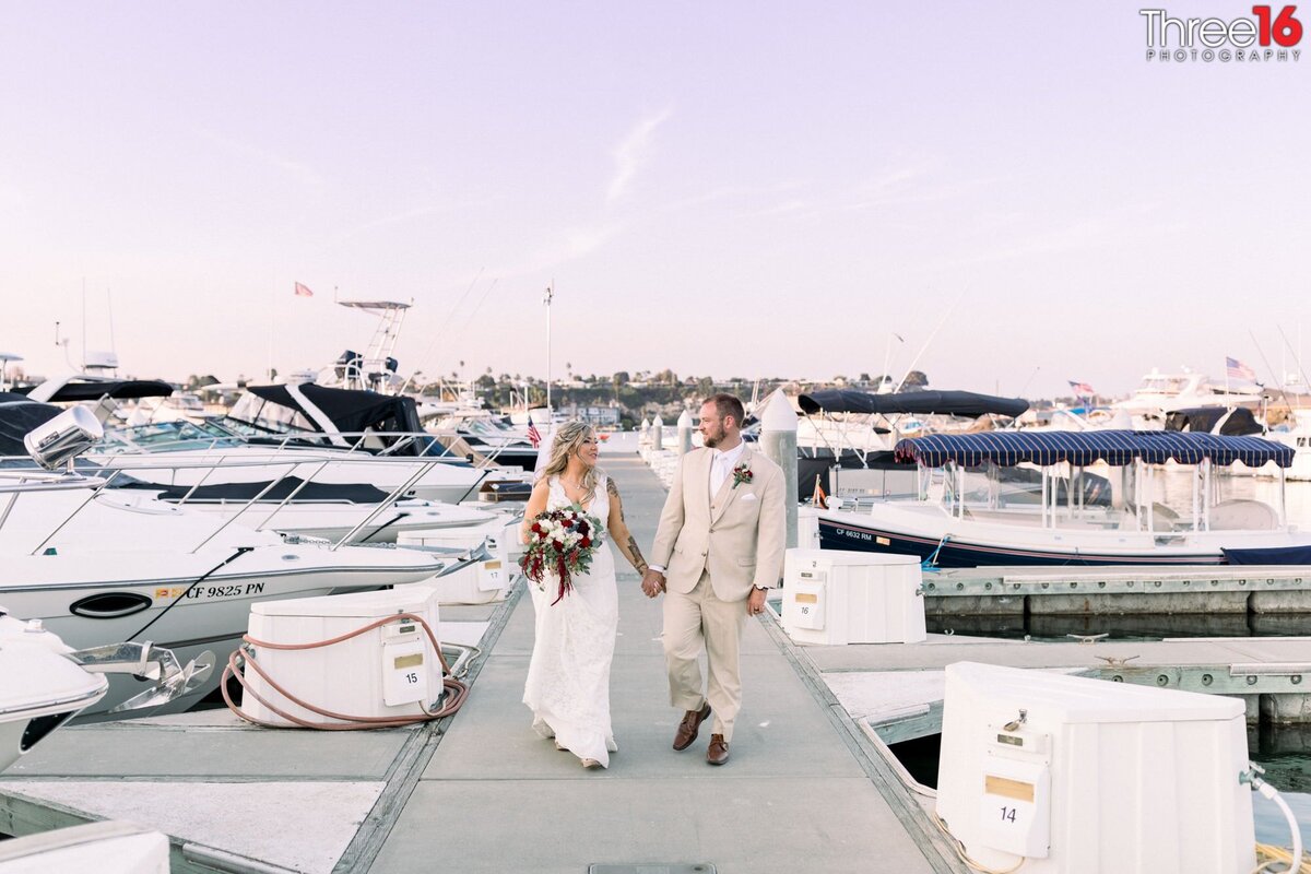 Bride and Groom walk hand in hand talking along the dock at the bay