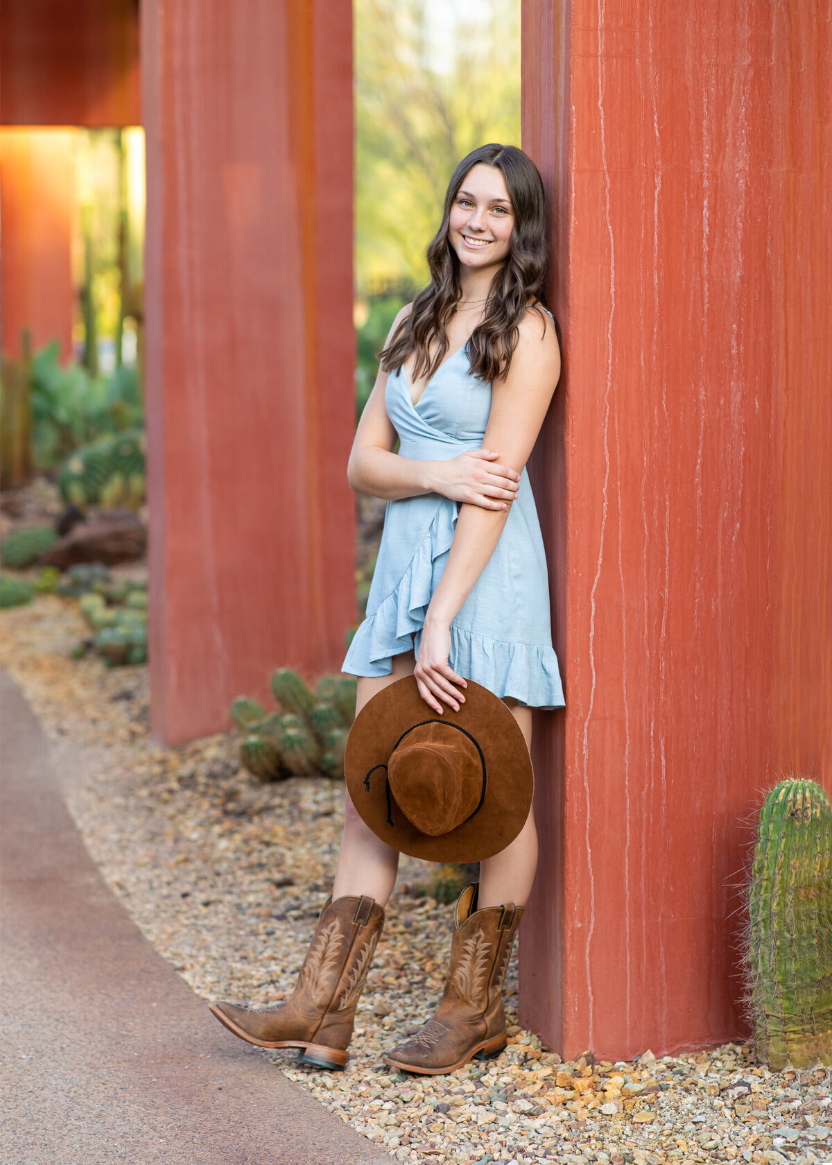 Senior girl in cowboy boots leaning against red wall