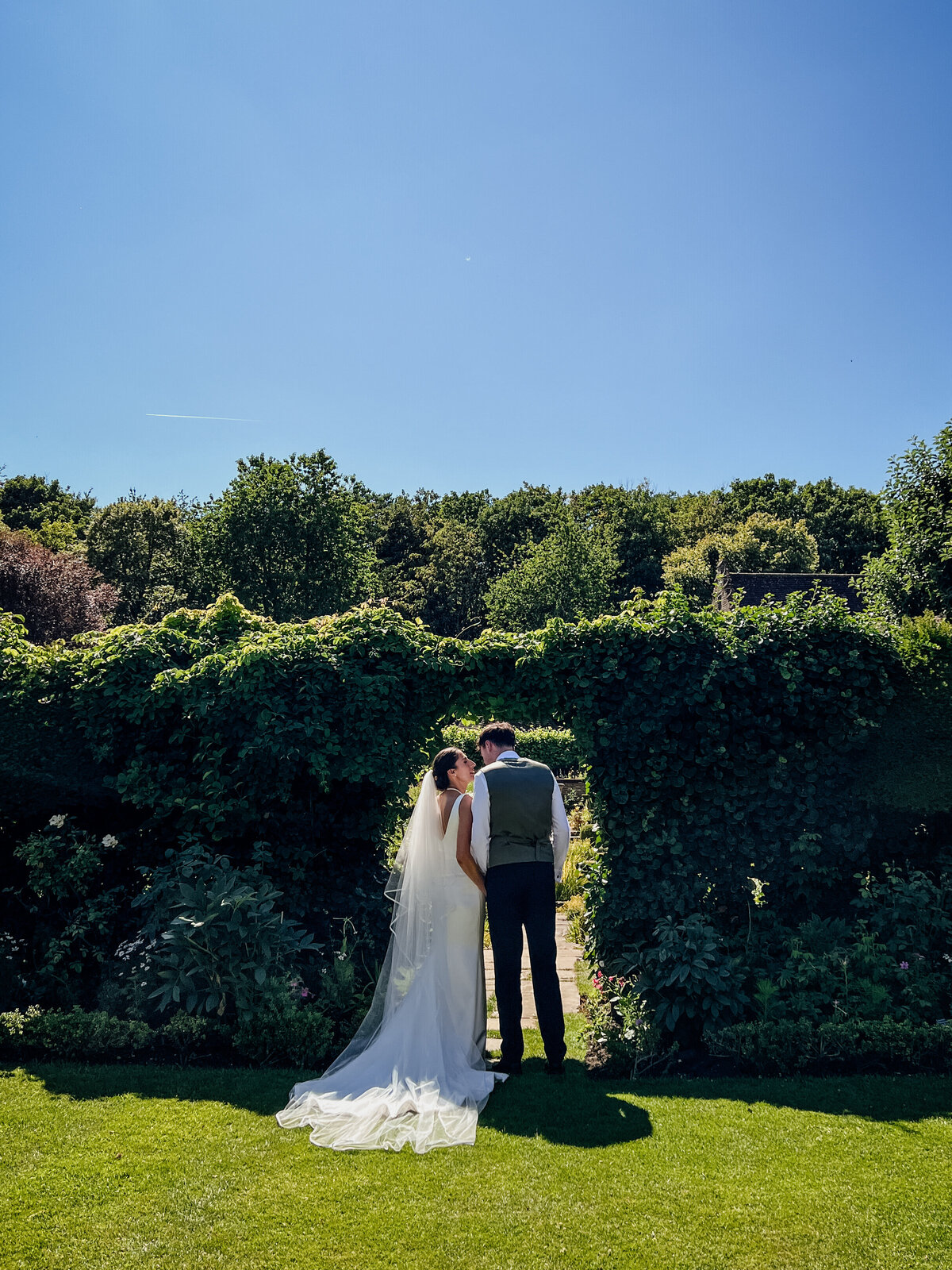 Bride and groom walking through garden sharing intimate moment away from guests captured by Suffolk Wedding Content Creator