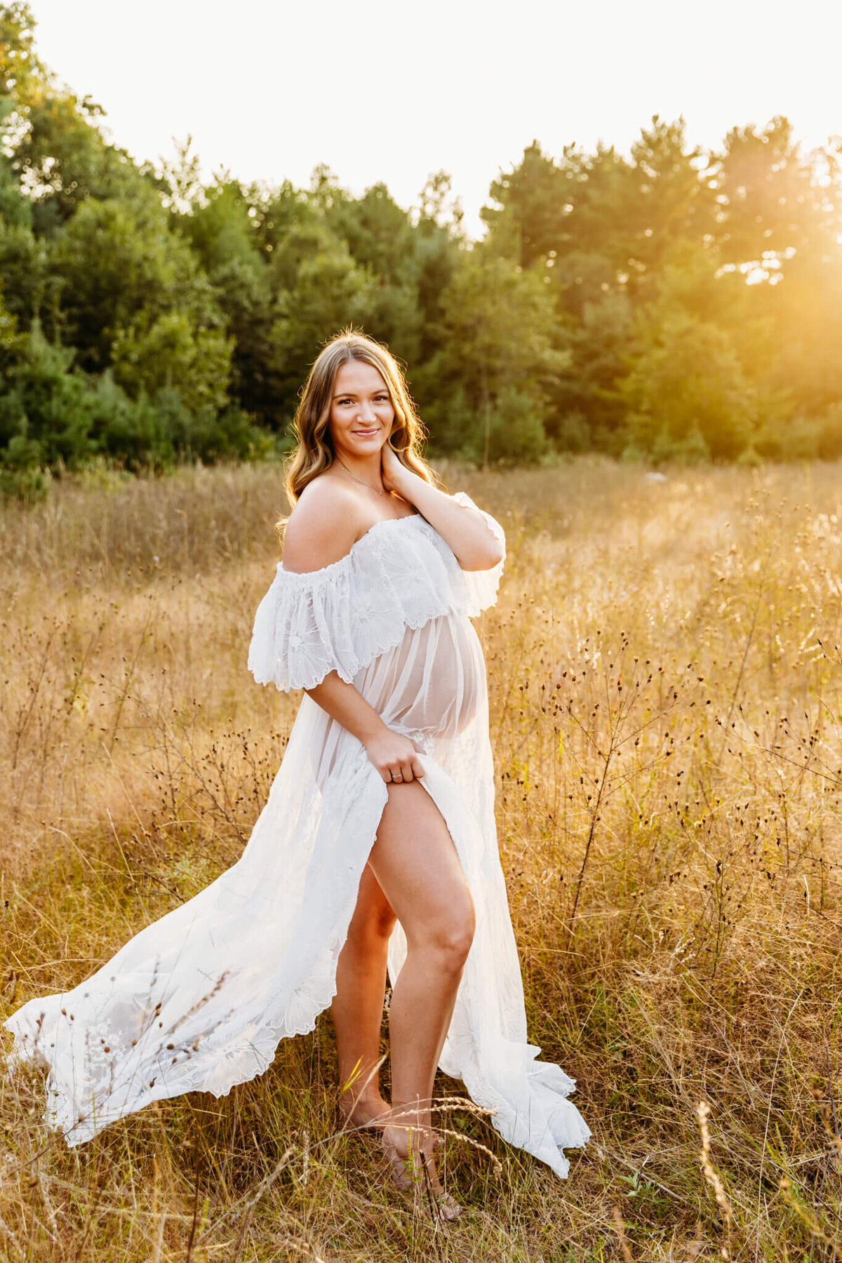 gorgeous mom to be in a floral lace gown standing with her leg showing in a beautiful field at golden hour near Green Bay