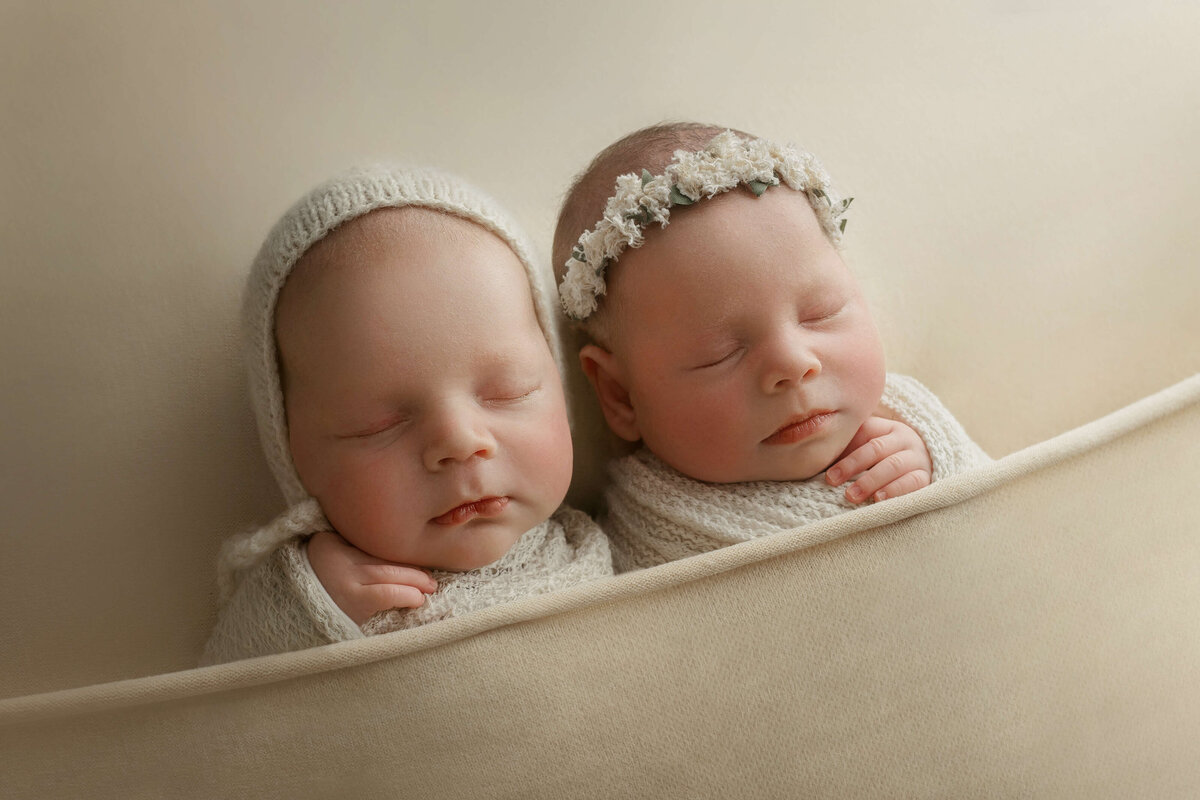 newborn twin babies laying together on a cream backdrop at their newborn photography session with a photographer at a loudoun county va photo studio