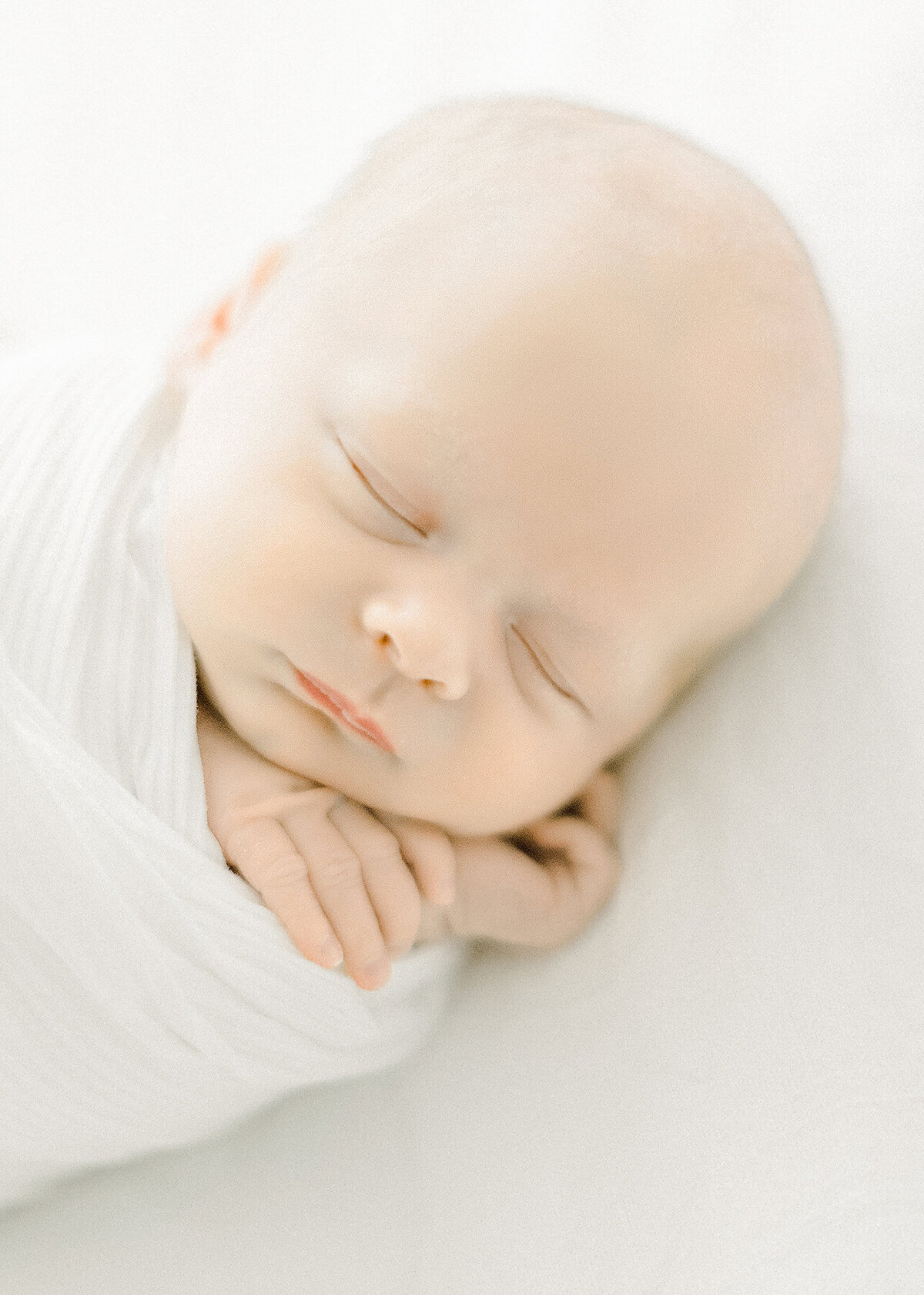 Close up detail photo of a newborn baby boy snuggled and wrapped as he sleeps with his hands by his face.