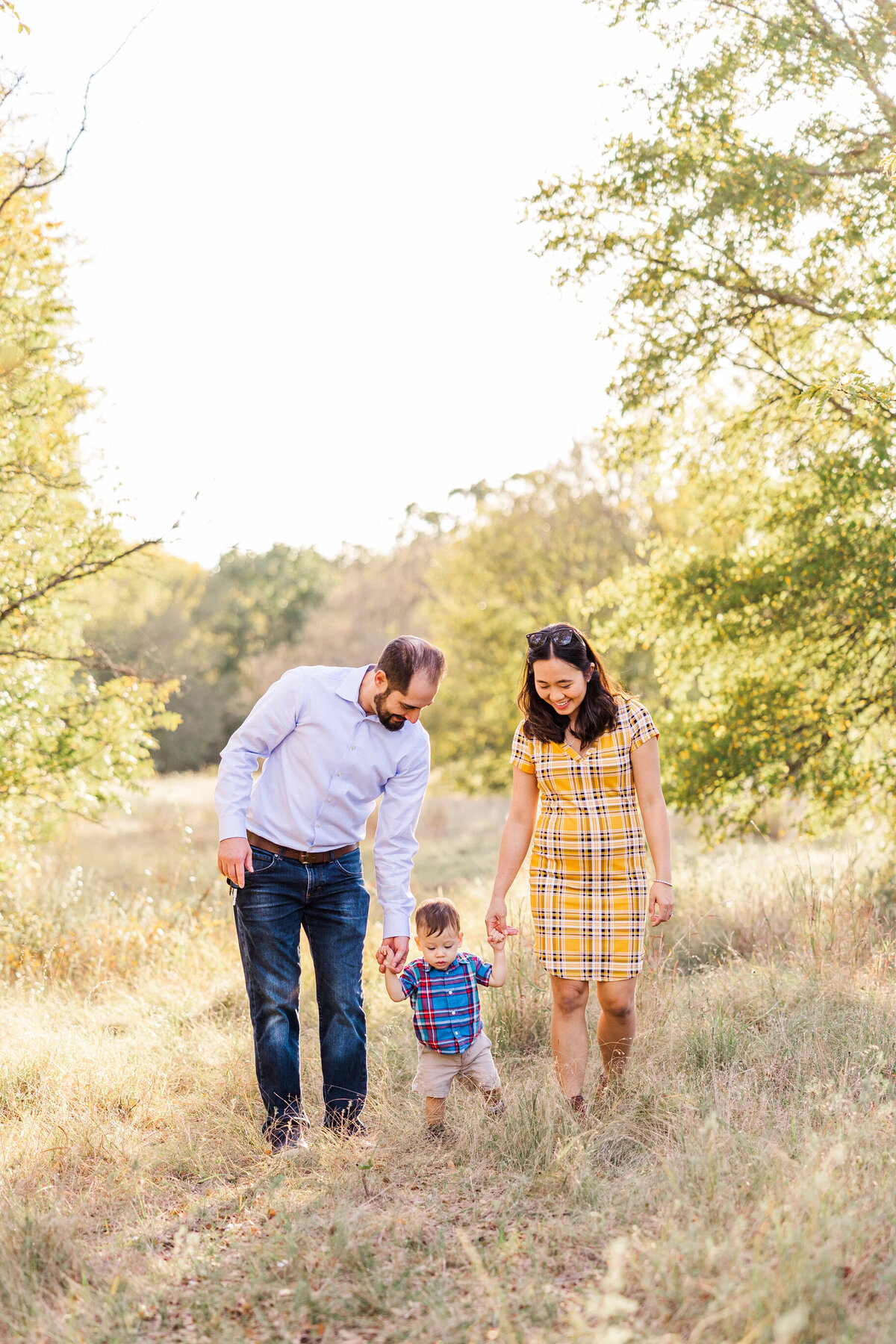 mom-and-dad-holding-1-year-olds-hand-while-waling-through-a-field-of-golden-yellow