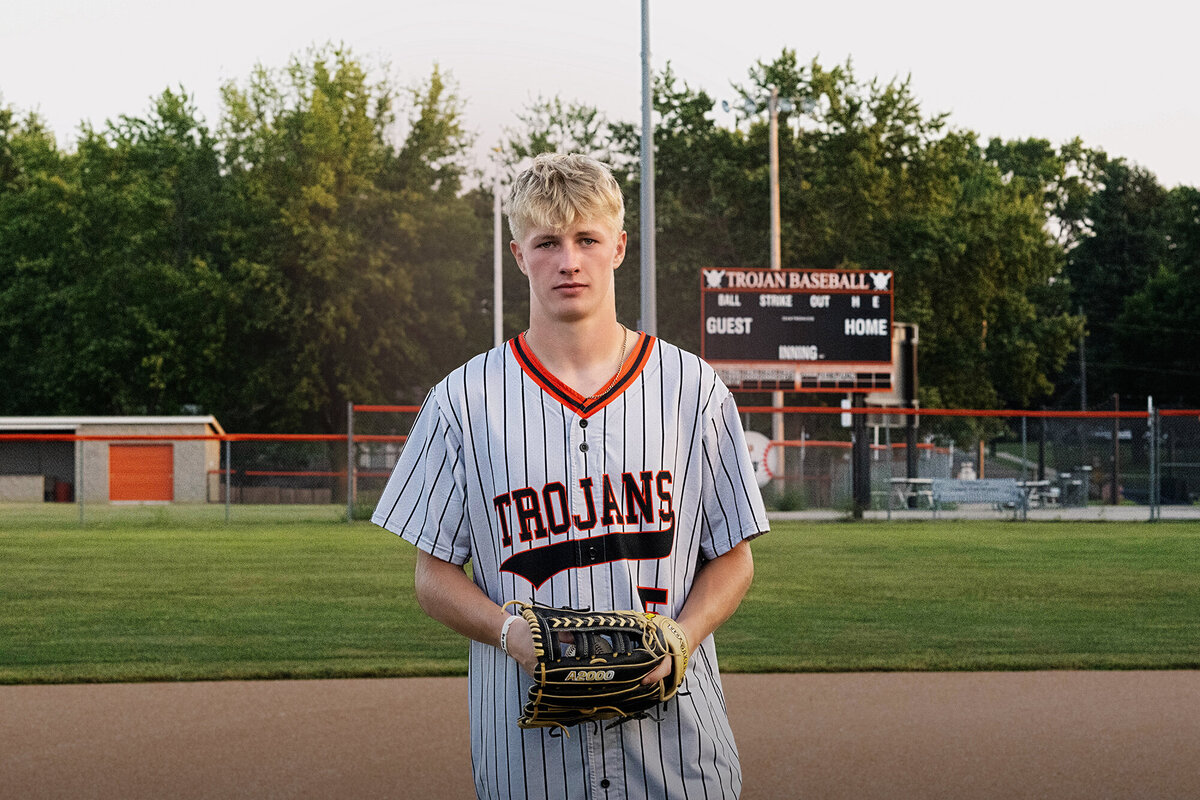 A high school baseball player standing in the field with glove and jersey