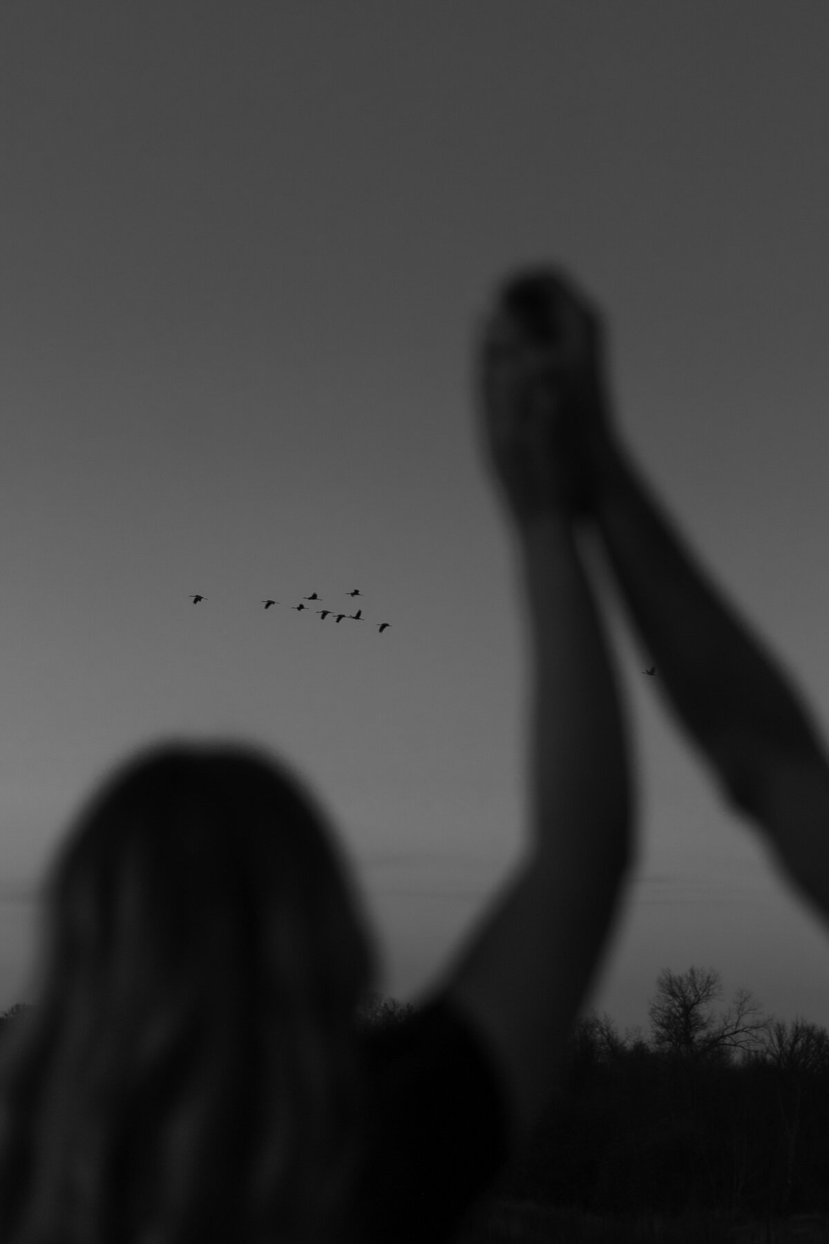 Black and white photo of couple spinning with birds flying behind them 