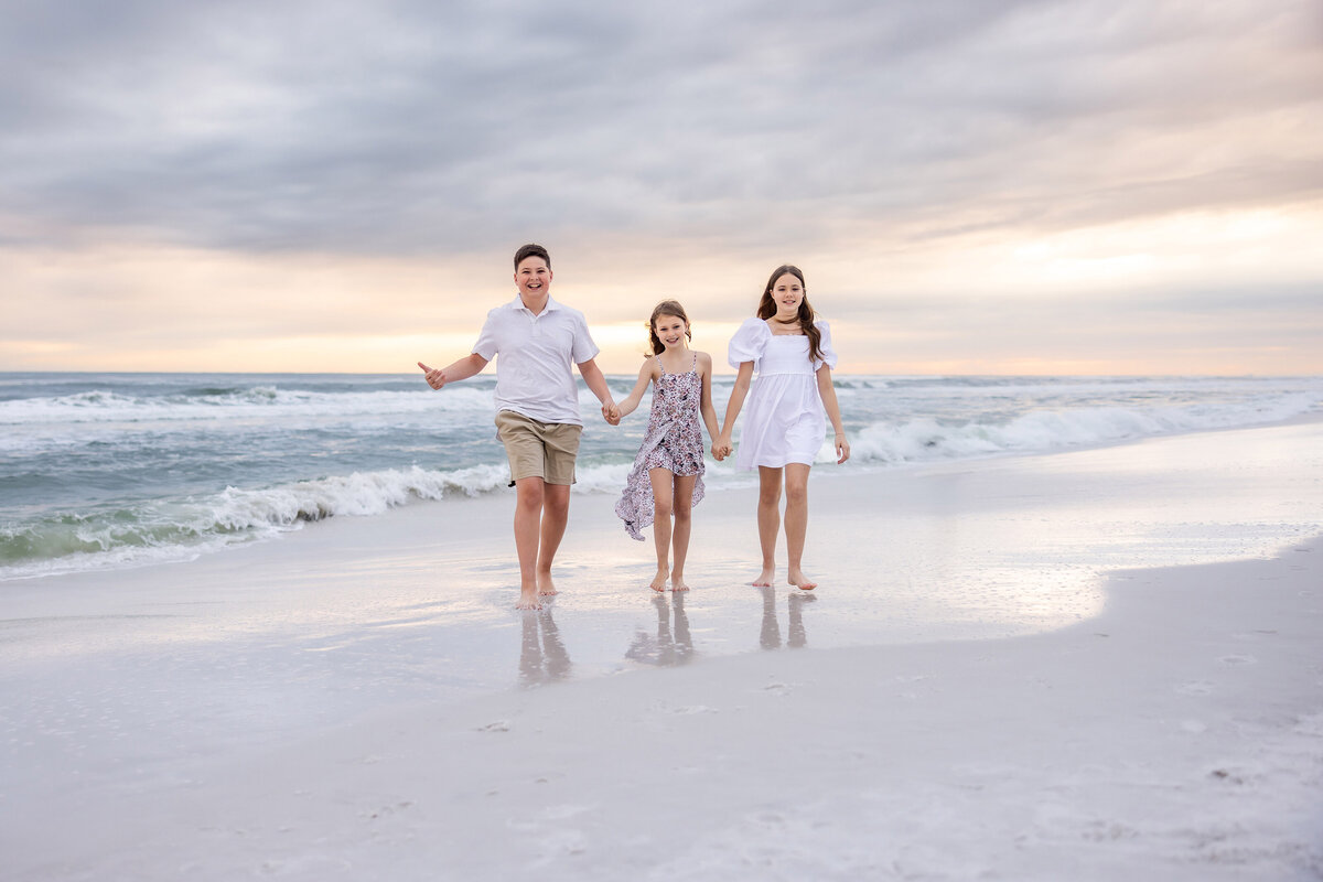 3 siblings holding hands running on beach in water on 30a
