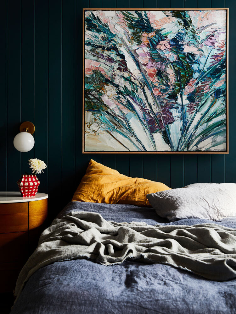Earthy abstract floral artwork above bed with navy panelled wall and stone side table in a calm bedroom setting.