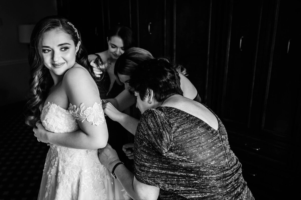 Several women help adjust a bride's wedding dress. Black and white.