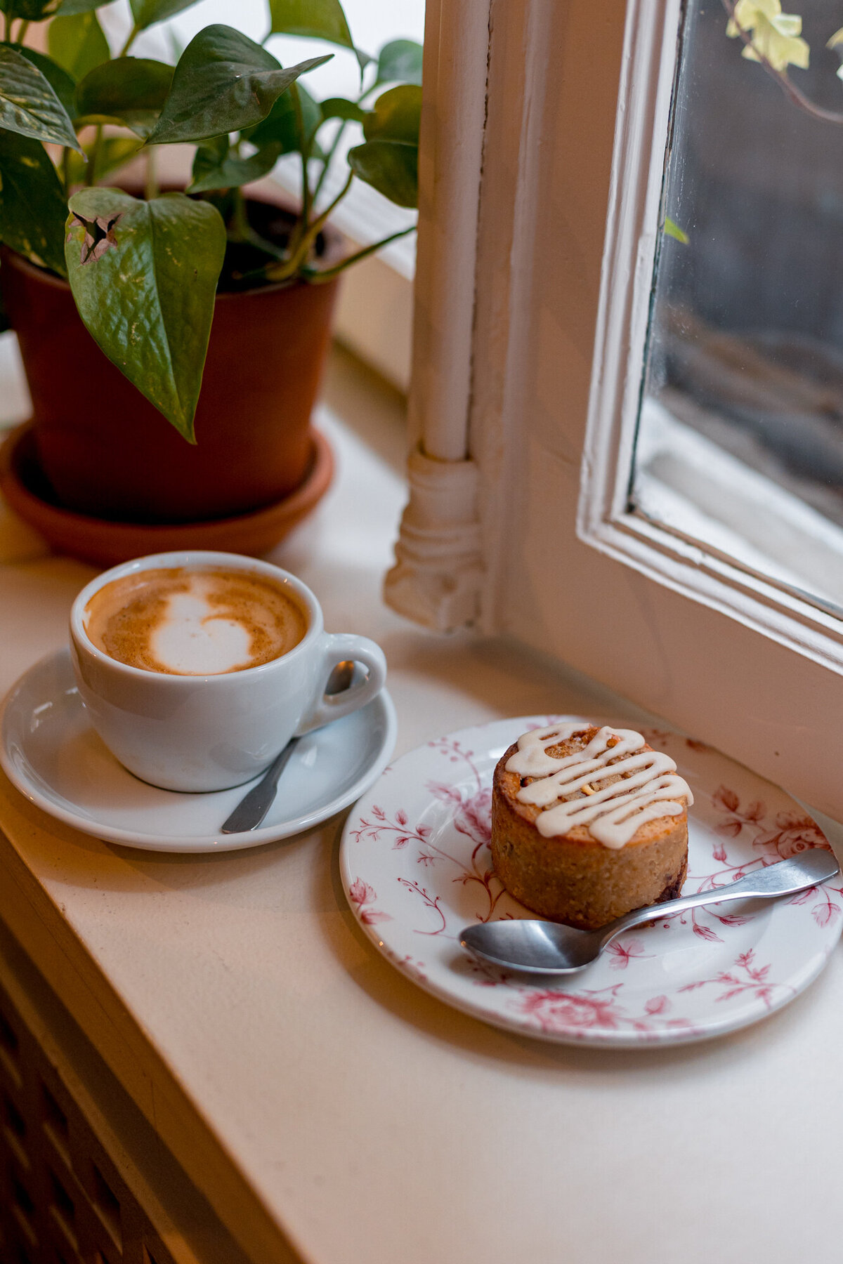 A Cinnamon bun and latte in front of a window