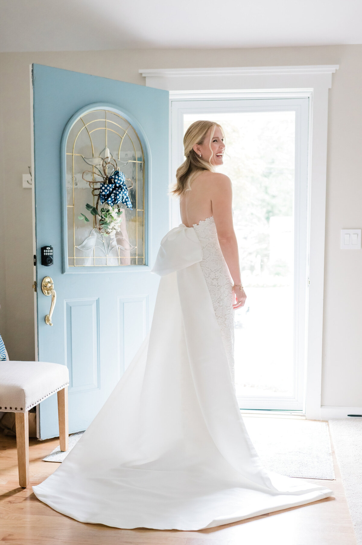 The bride stands in front of a blue door with stained glass details, beaming as she looks back.
