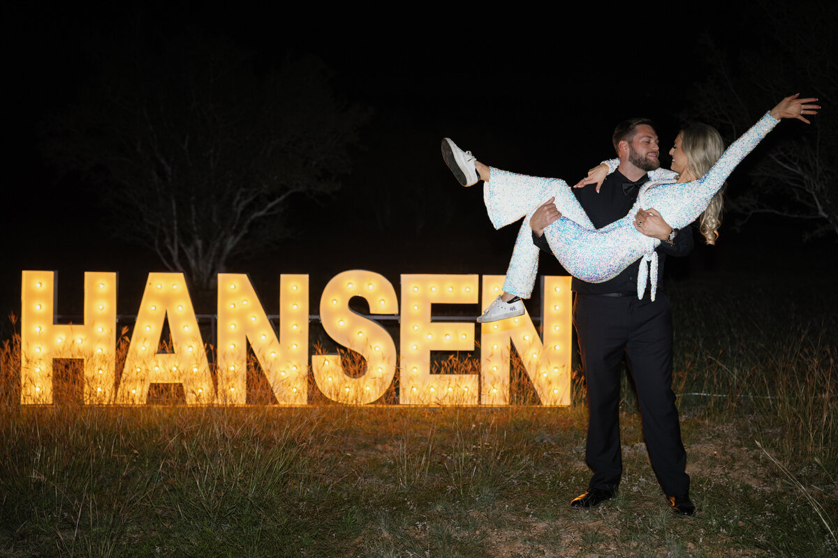 groom lifts bride in front of wedding sign