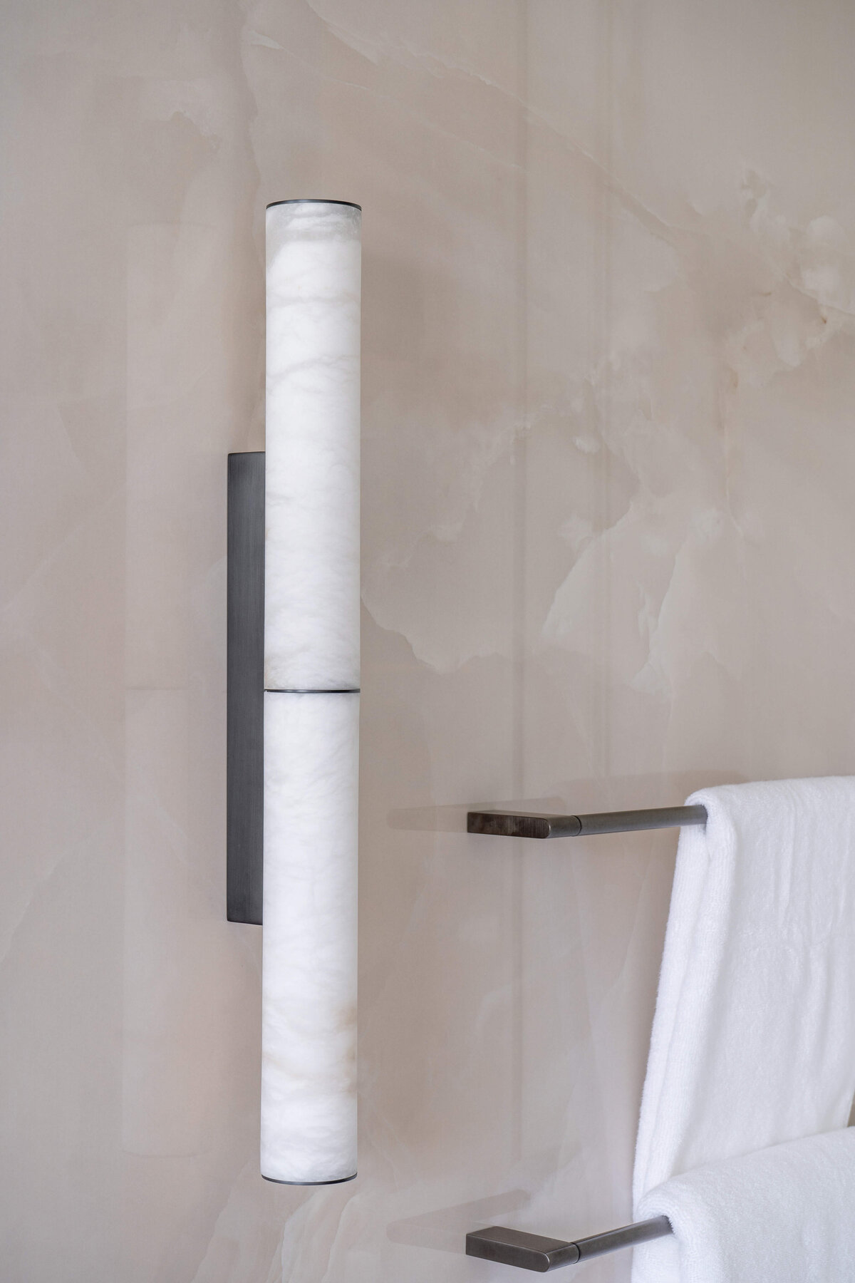 Cylindrical white sconces  on a neutral marble wall in a light, airy primary bathroom.