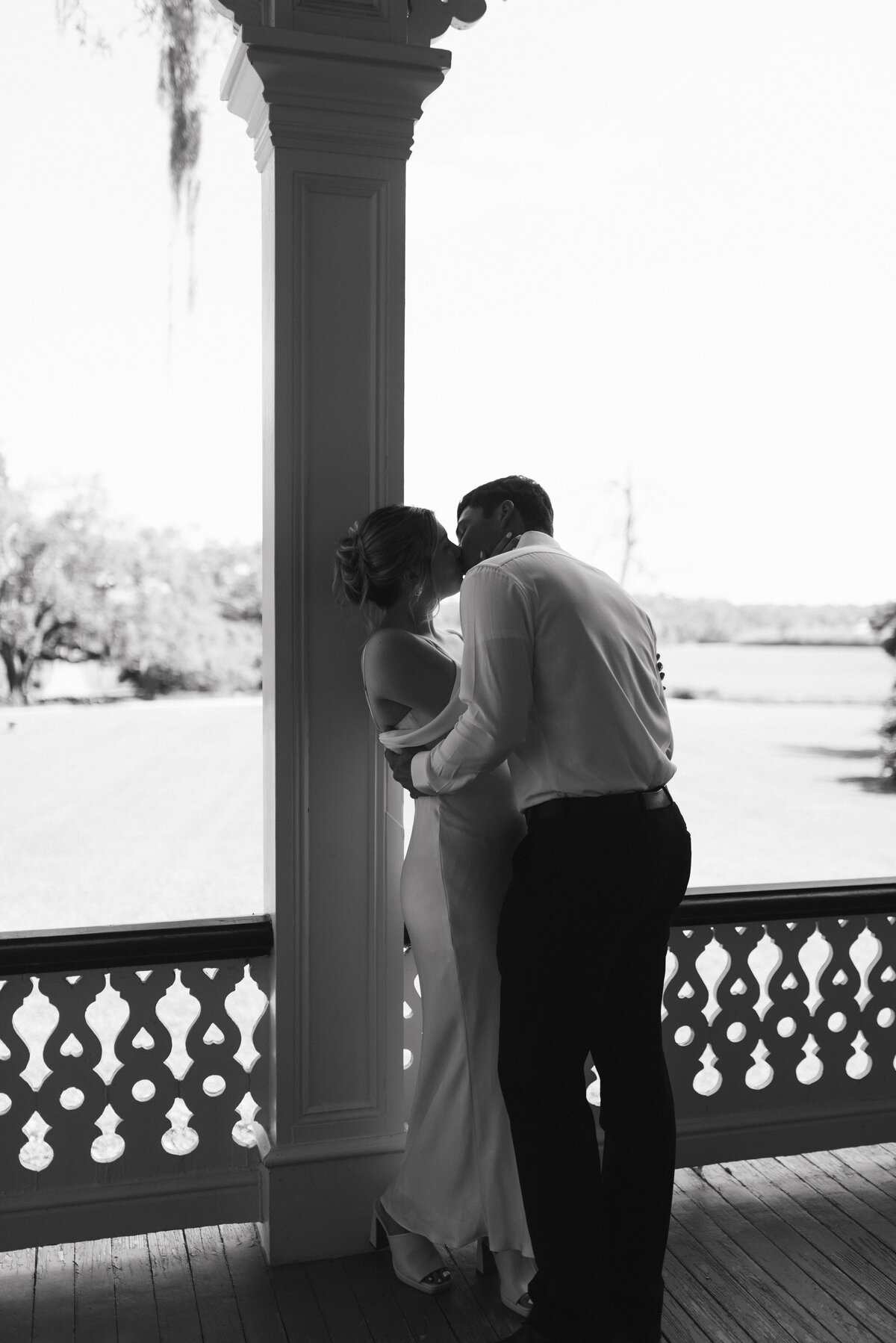 a black and white photo of a couple kissing on the porch of the jefferson house at rip van winkle gardens in louisiana. 