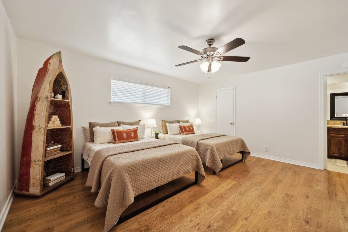 Spacious guest bedroom at 3120 Chapel Downs Dr Dallas TX featuring double beds, hardwood flooring, neutral decor, and vintage bookshelf — listed by Haven Realty Group.
