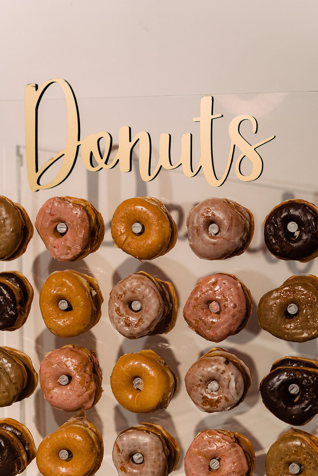 A wall-mounted display of assorted donuts with a sign reading “Donuts” above, offering various glazes from chocolate to pink icing as a fun dessert option for guests.