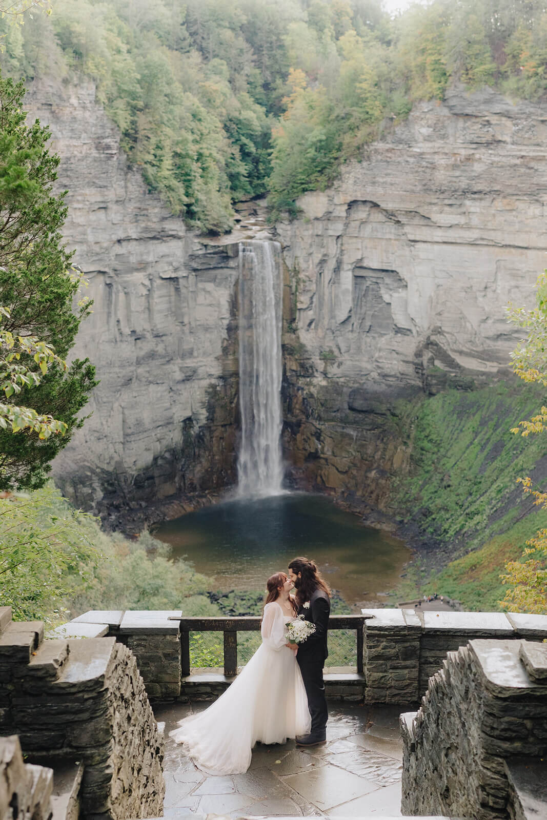bride and groom standing in front of a waterfall