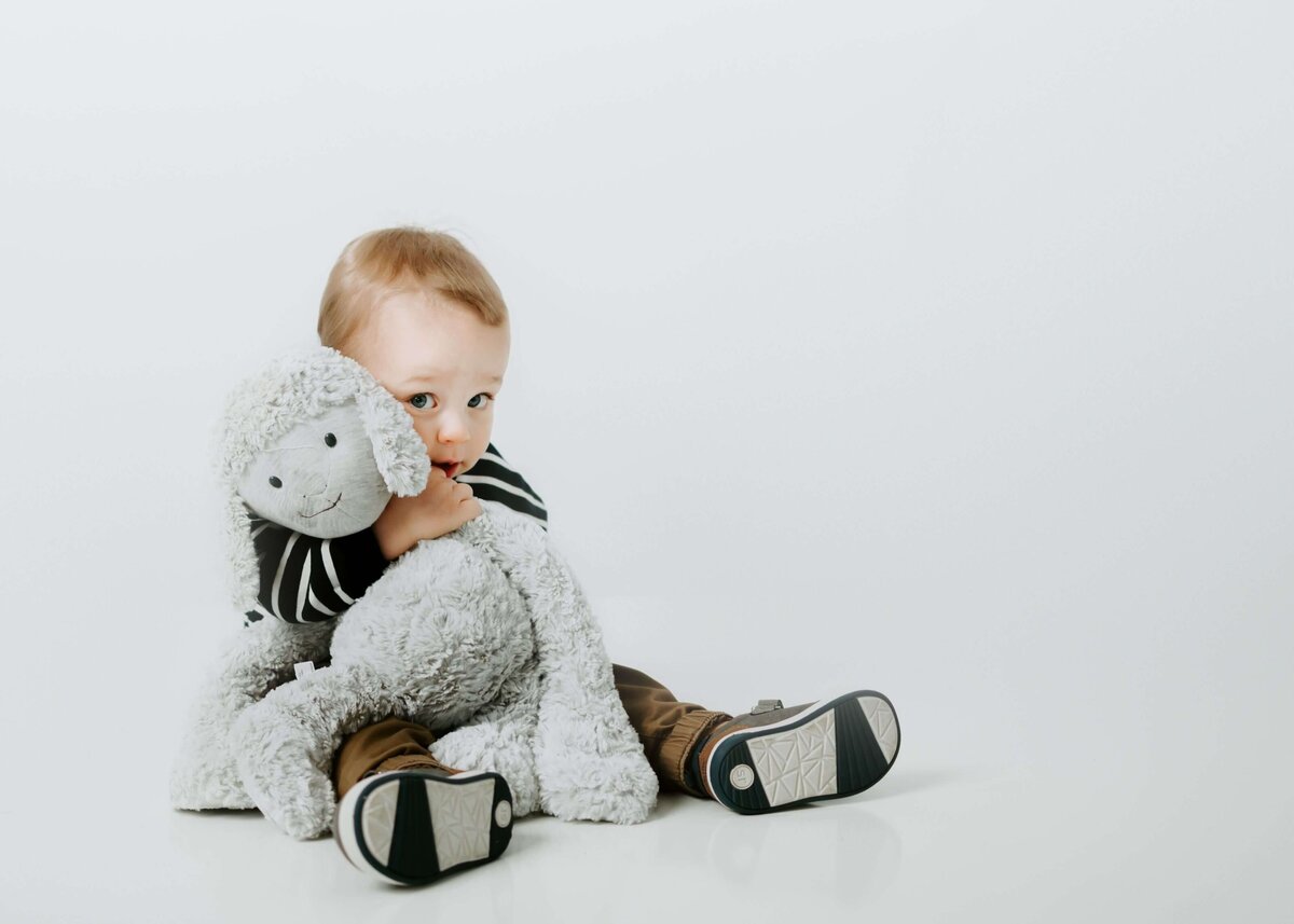 A baby is happily playing with a stuffed animal on a white background. Capture this precious moment with the expertise of a Pittsburgh family photographer.
