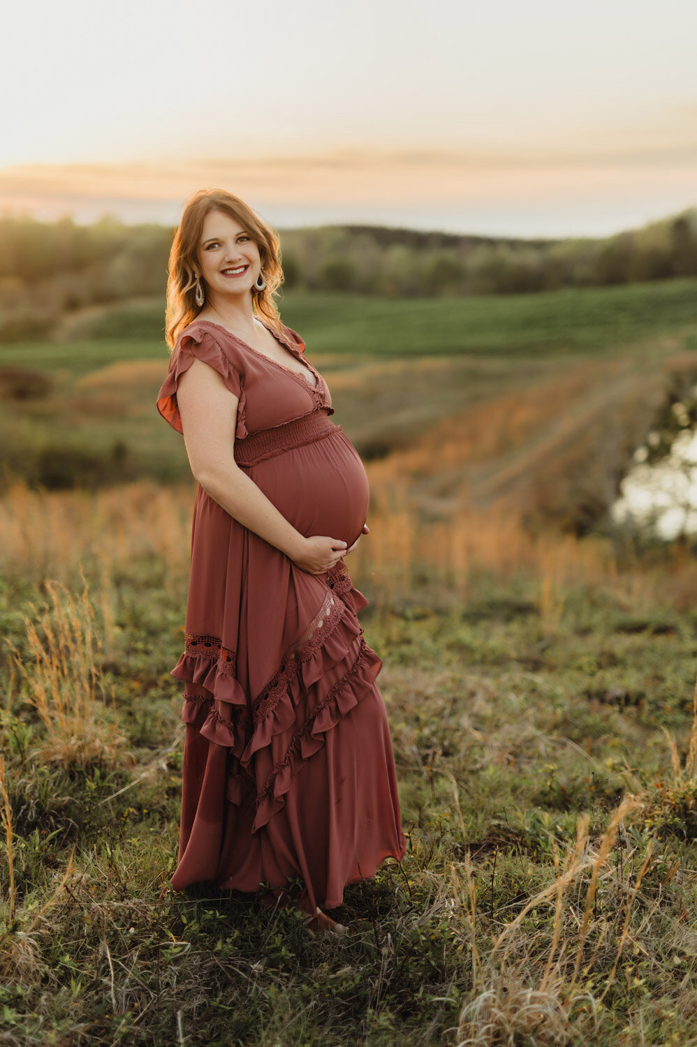 Joyful expecting mother in rust maternity gown during sunset photo session in Greensboro NC