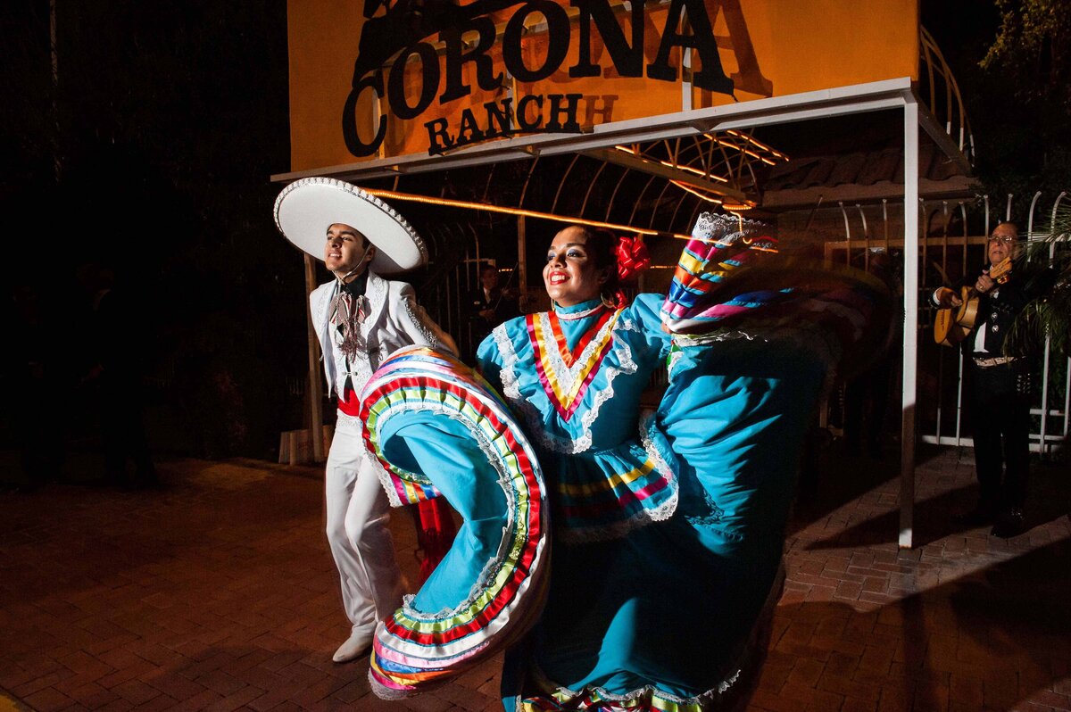 A women dressed in colorful outfit twirls as man dances with Mexican outfit at Corona Ranch