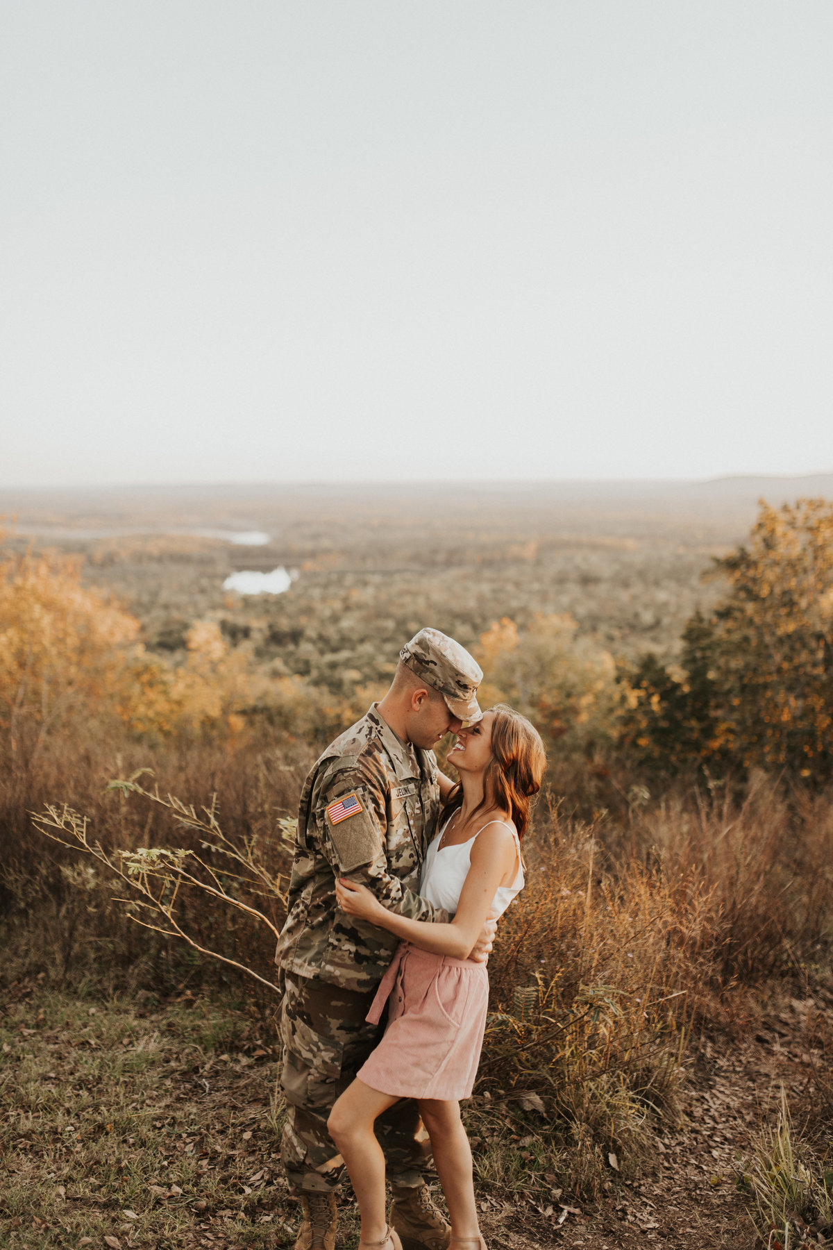 engaged couple standing outside, man is in a military outfit, woman is in a white top and pink shorts