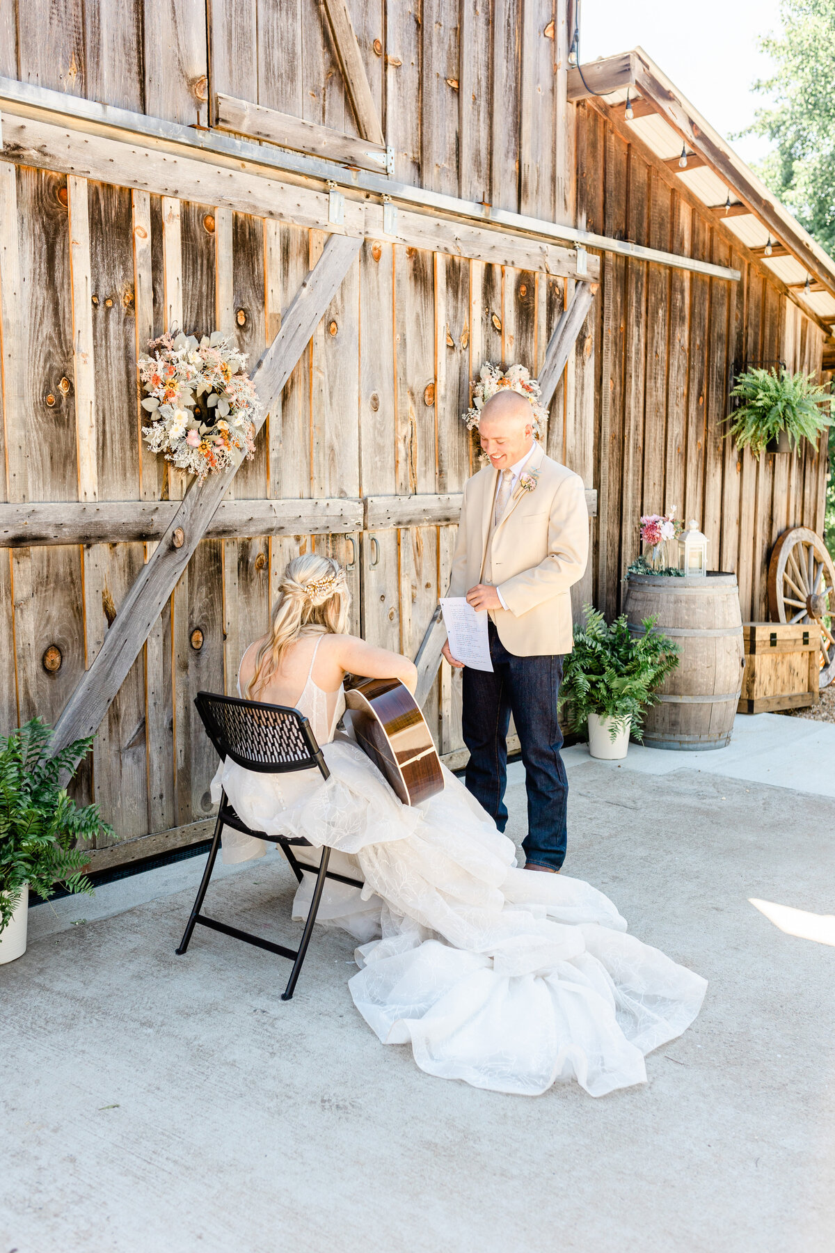 bride playing her guitar and singing to the groom in front of a barn door