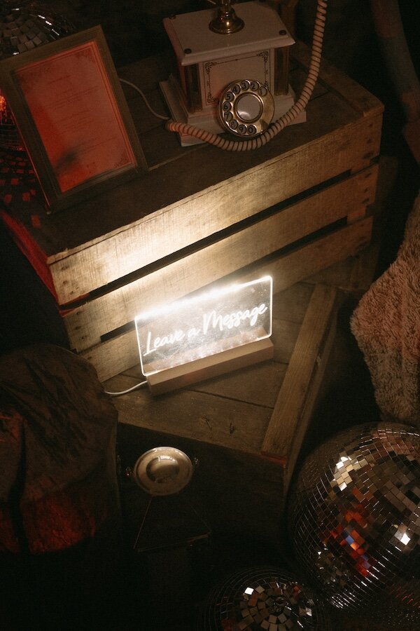 Boule à facette, téléphone vintage sur caisse en bois et néon "Laisser un message" dans un décor feutré. Ambiance rétro capturée par Kamescop.