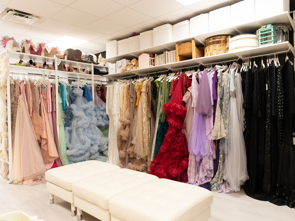 A vibrant dressing room with colorful gowns hanging on racks, organized by hue. Shelves above hold various shoes and storage boxes, conveying elegance and variety.