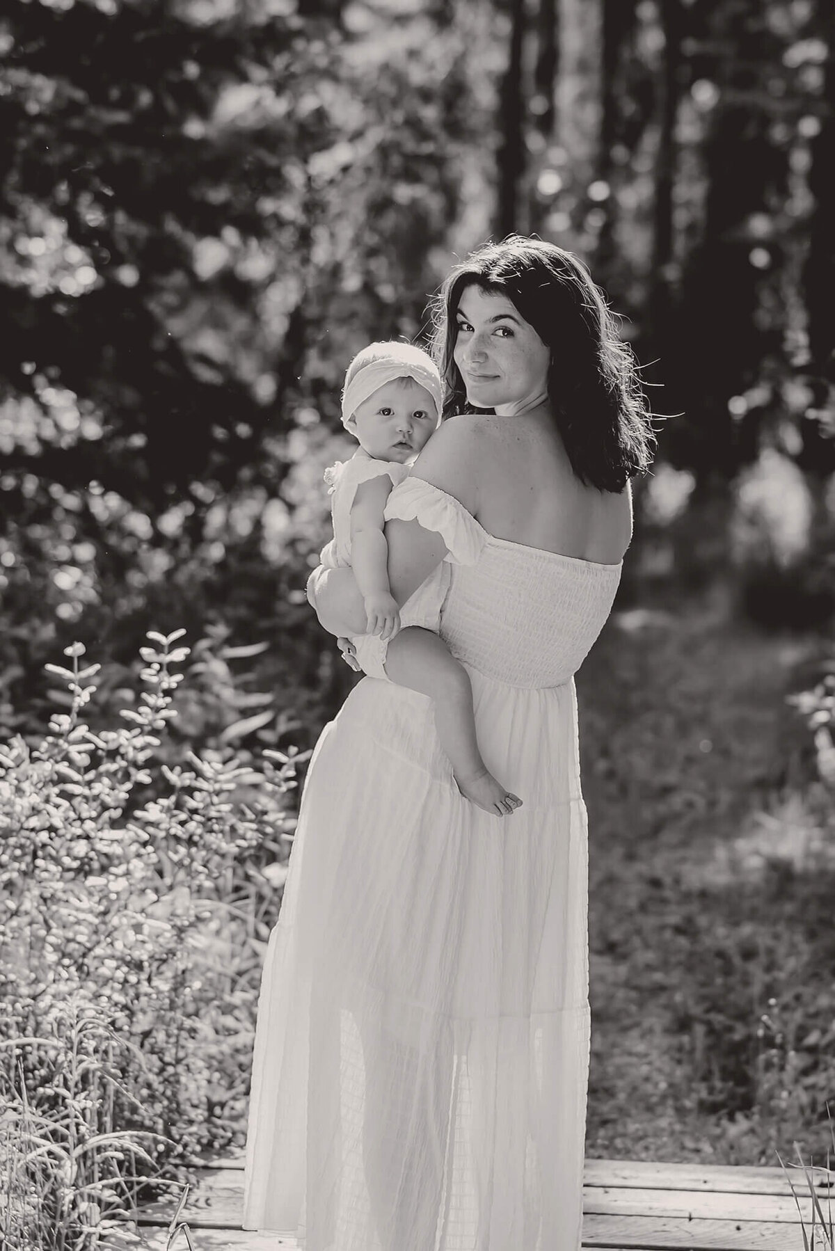 A mother and daughter stand in the forest being backlit by beautiful sun. This black and white portrait is taken by Brittany Danielle