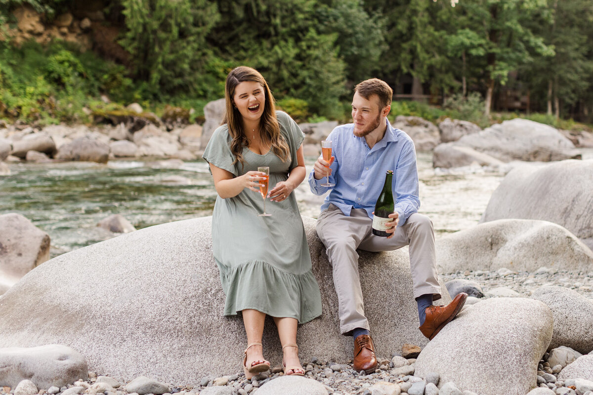PNW mountain river engagement session Stevens Pass at Snohomish river couple popping champagne fun candid photo by Joanna Monger Photography