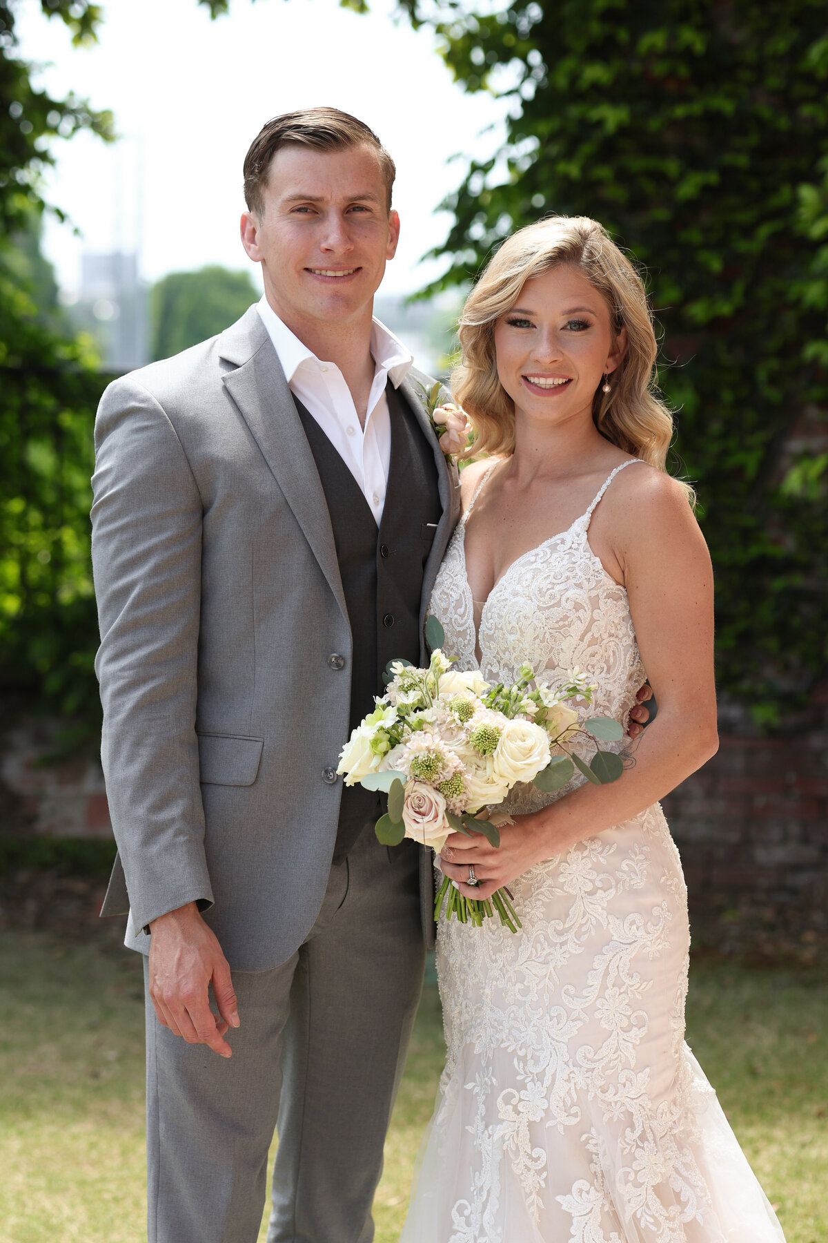 bride and groom standing next to each other wearing gray suite and white lace dress at The Bibb Mill in Columbus Georgia by Columbus Georgia wedding photographer Amanda Richardson Photography