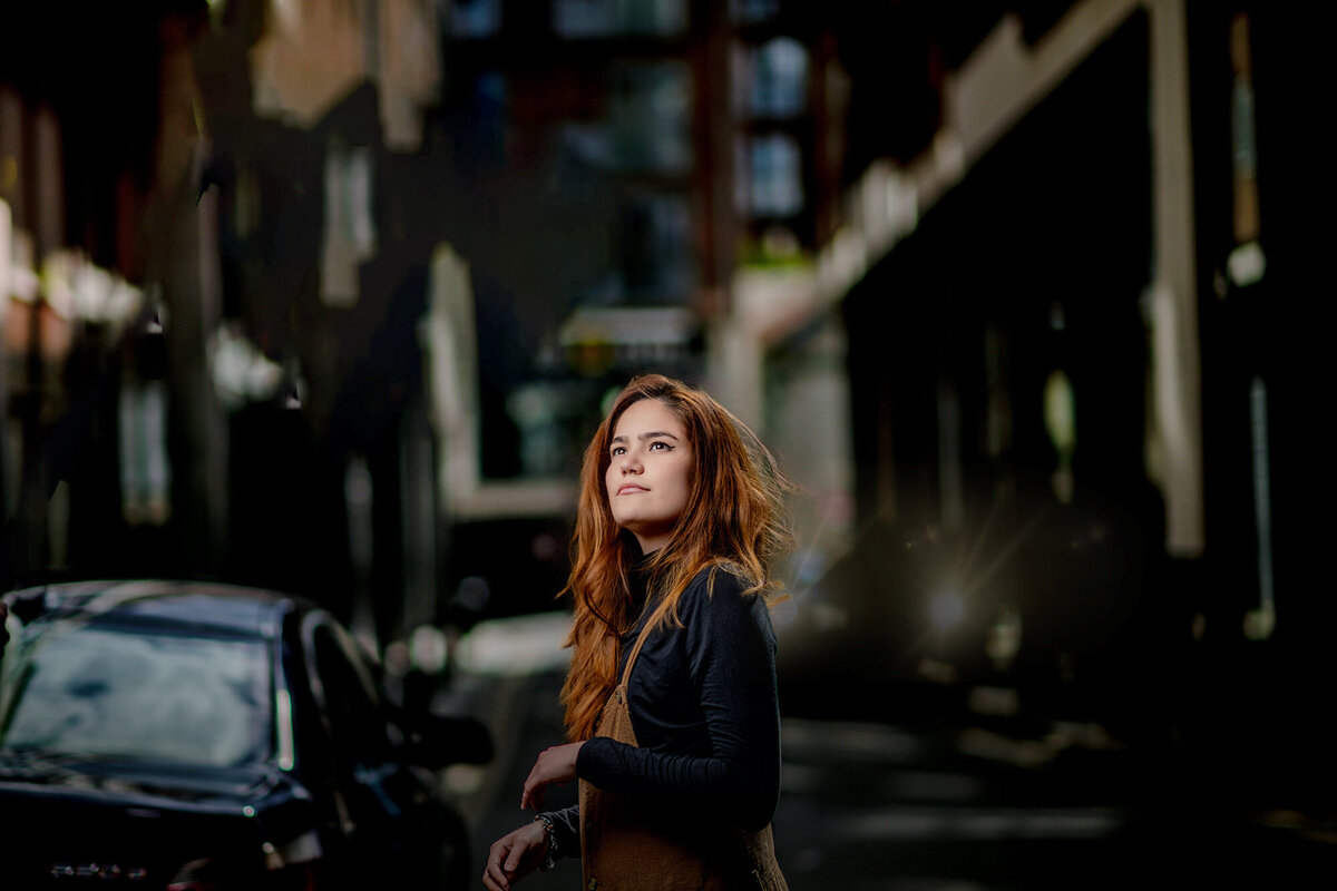 A woman with red hair gazes up while walking in the street in a black shirt for her Pella Senior Photographer