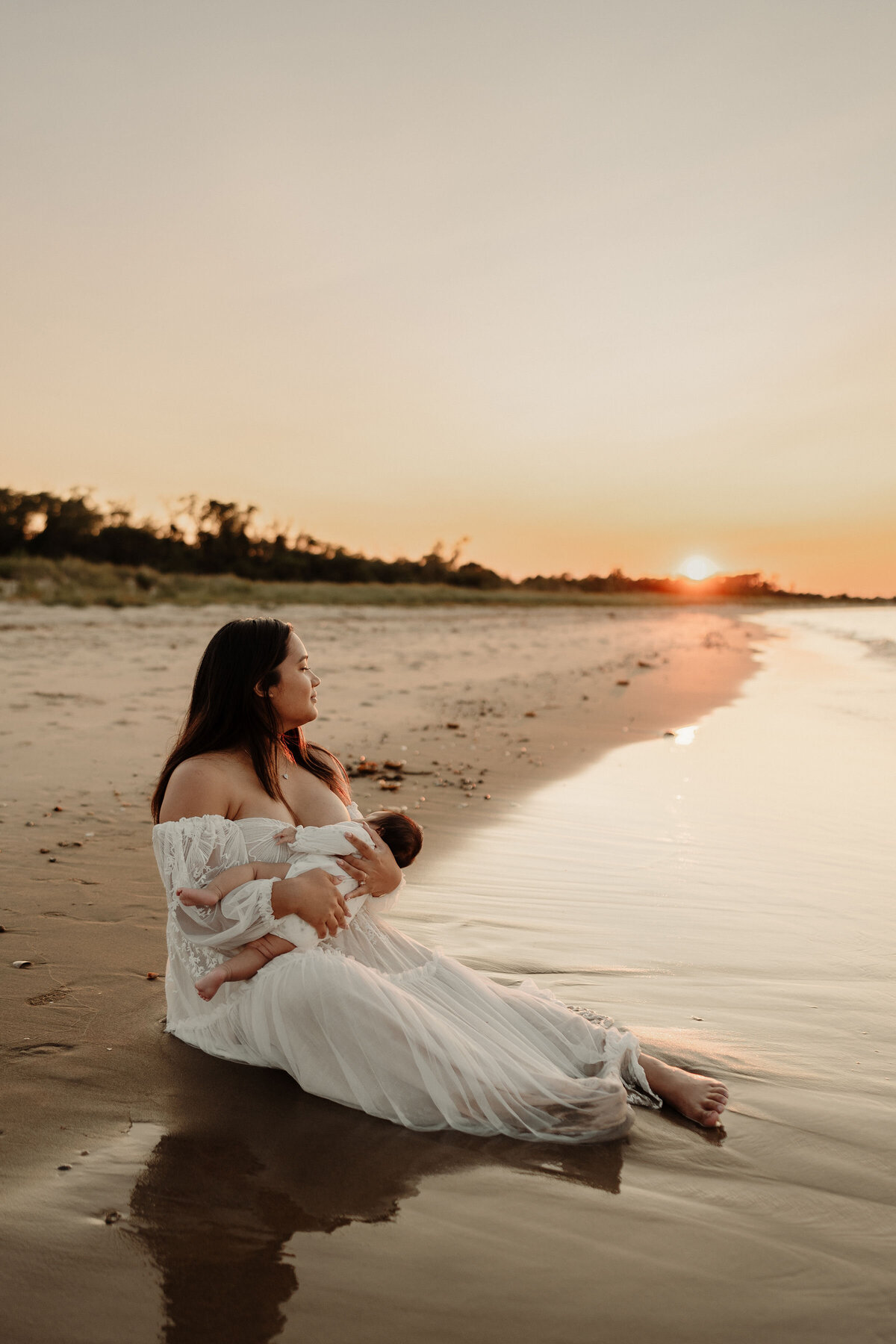 Mom breastfeeding baby on a beach at sunset
