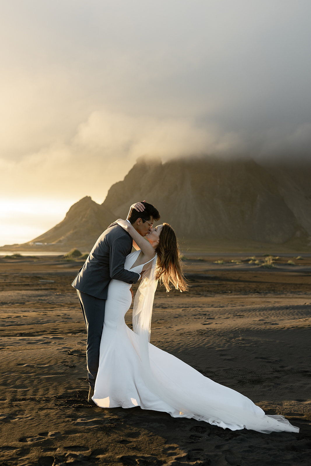 Couple kissing at sunset on the black sand beach in Iceland with dramatic mountains, photographed by a destination elopement photographer.
