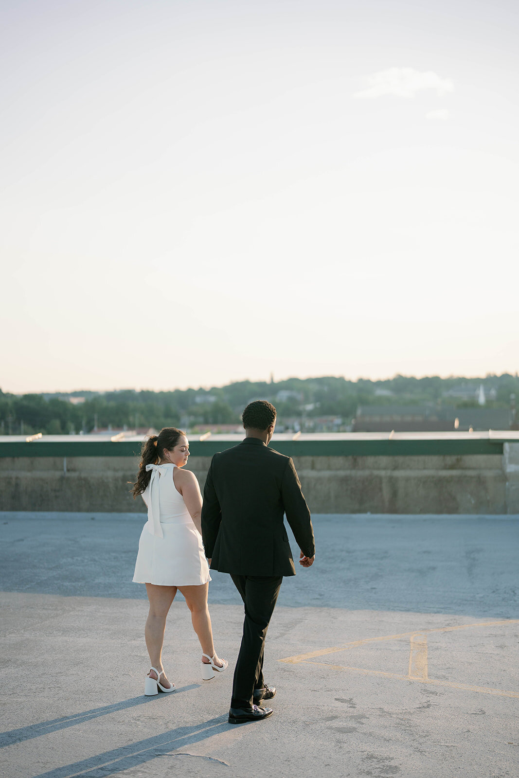 Dreamy sunset engagement photo of couple walking across a Kalamazoo rooftop.