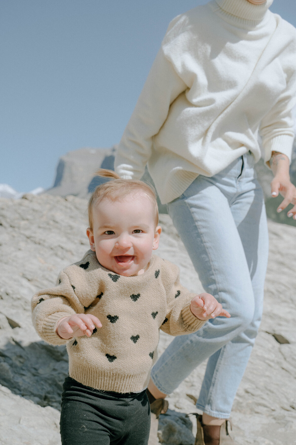 Mother walks toddler beside scenic lake on sunny day in Banff.