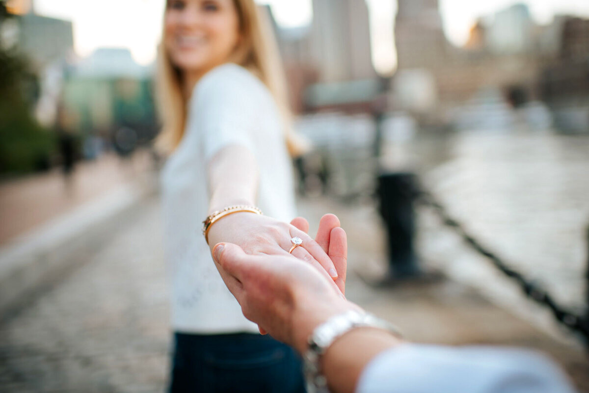 engaged couple holding hands with diamond ring in seaport district boston harbor