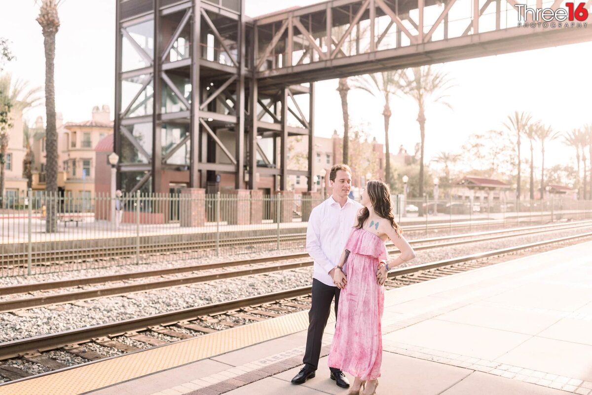Engaged couple hold hands next to the Fullerton Train Station tracks