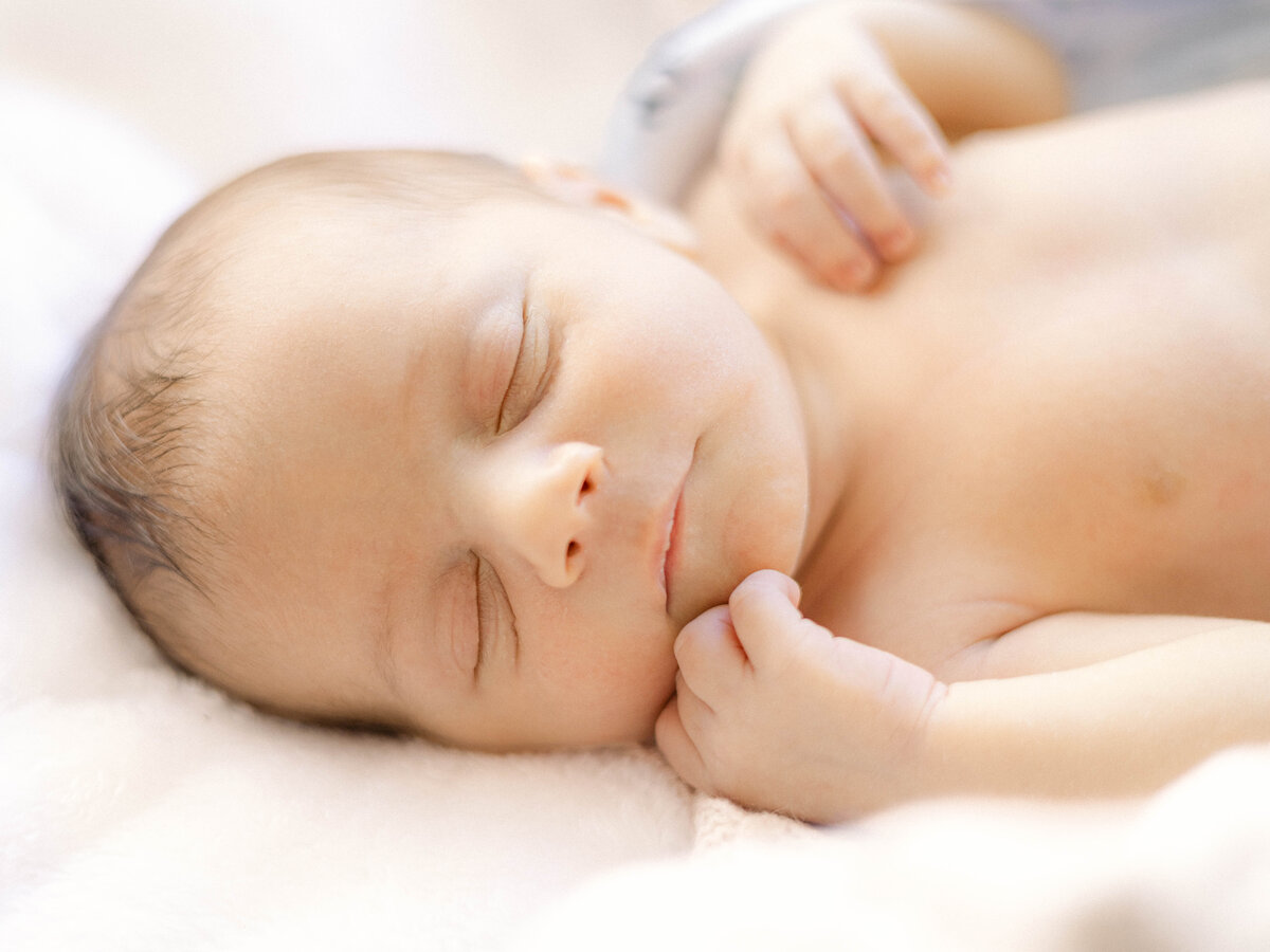 Newborn swaddled in white cotton blanket, resting in the nursery.