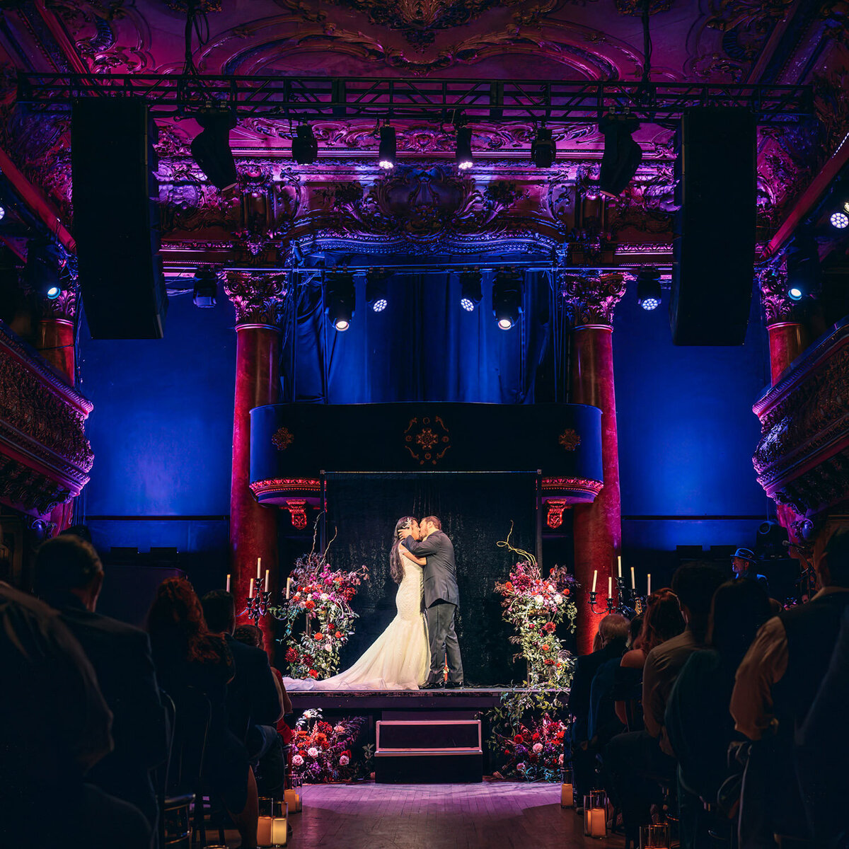 Indoor wedding ceremony with bold floral arrangements under purple lighting