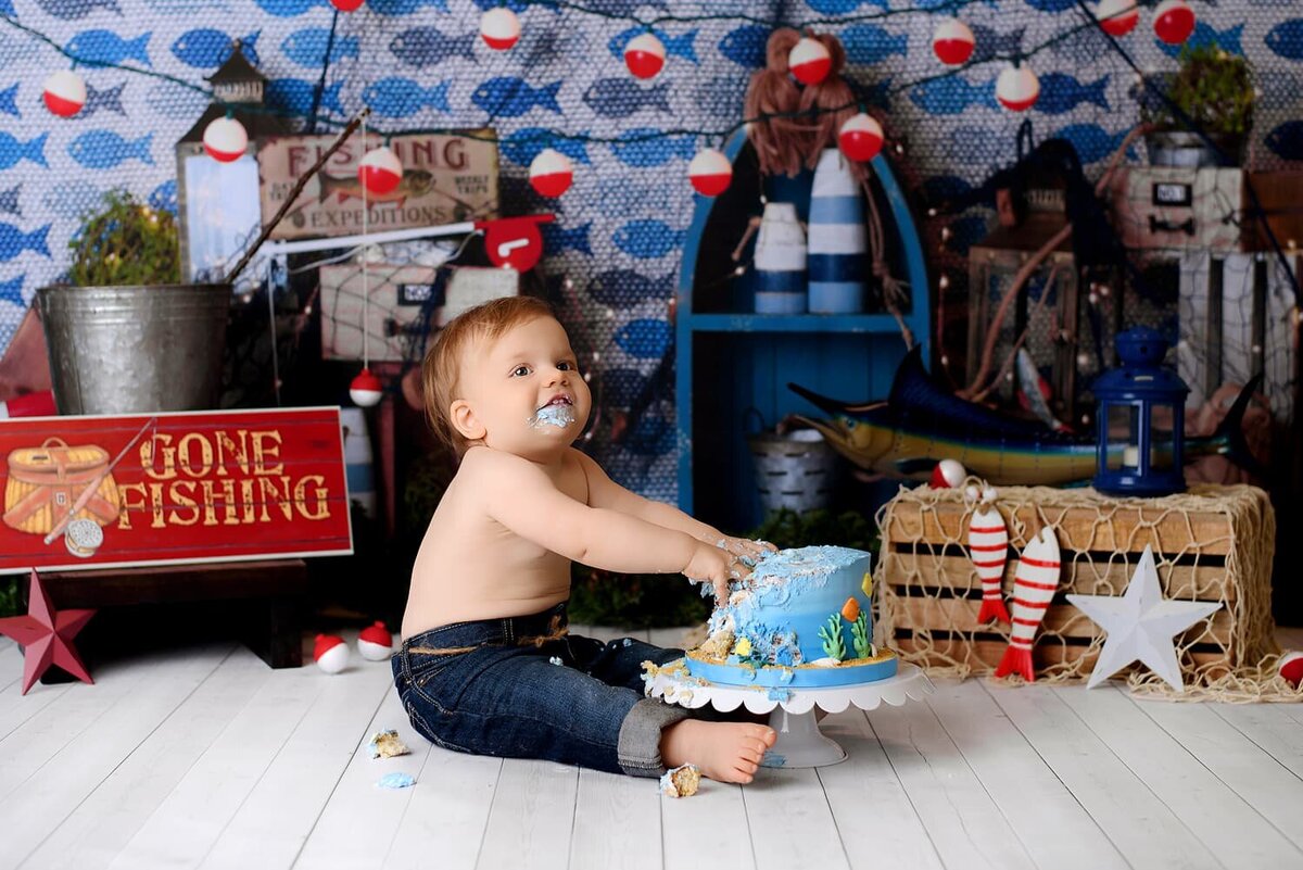 Baby boy in denim jeans  with blue and red fishing theme backdrop.