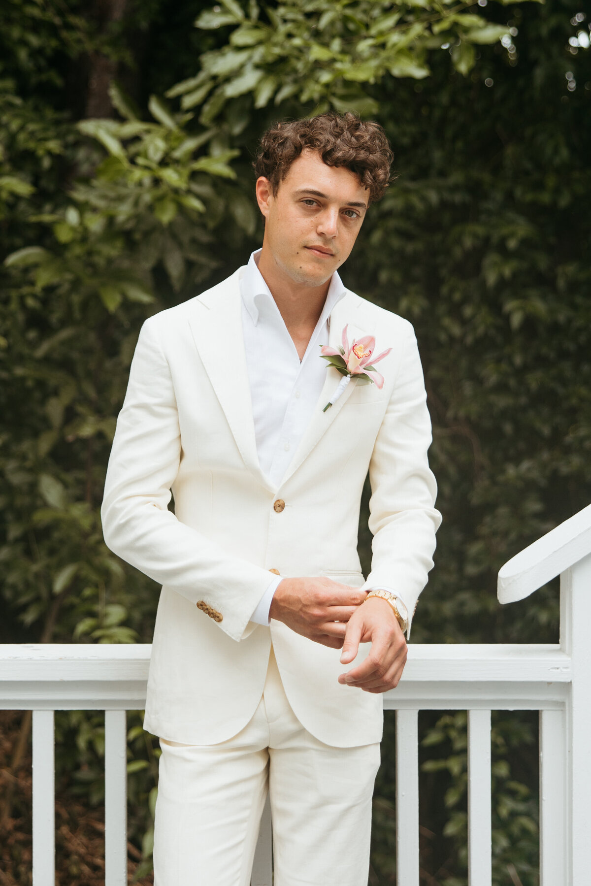 Groom in a white suit adjusting his jacket, looking directly at the camera