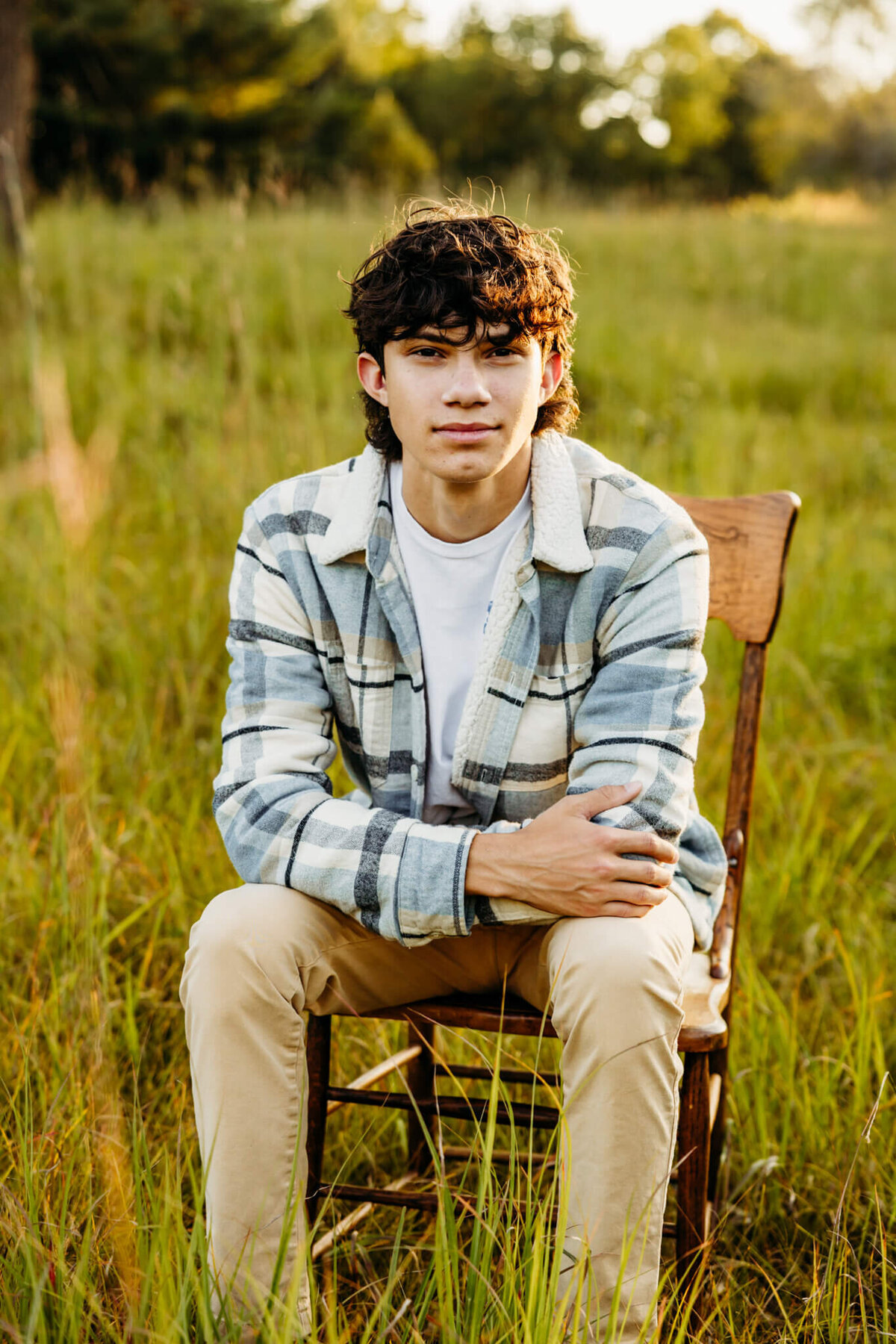 teen boy in a blue plaid jacket sitting with his arms on his legs and looking serious as he sits on a chair captured by Ashley Kalbus Photography