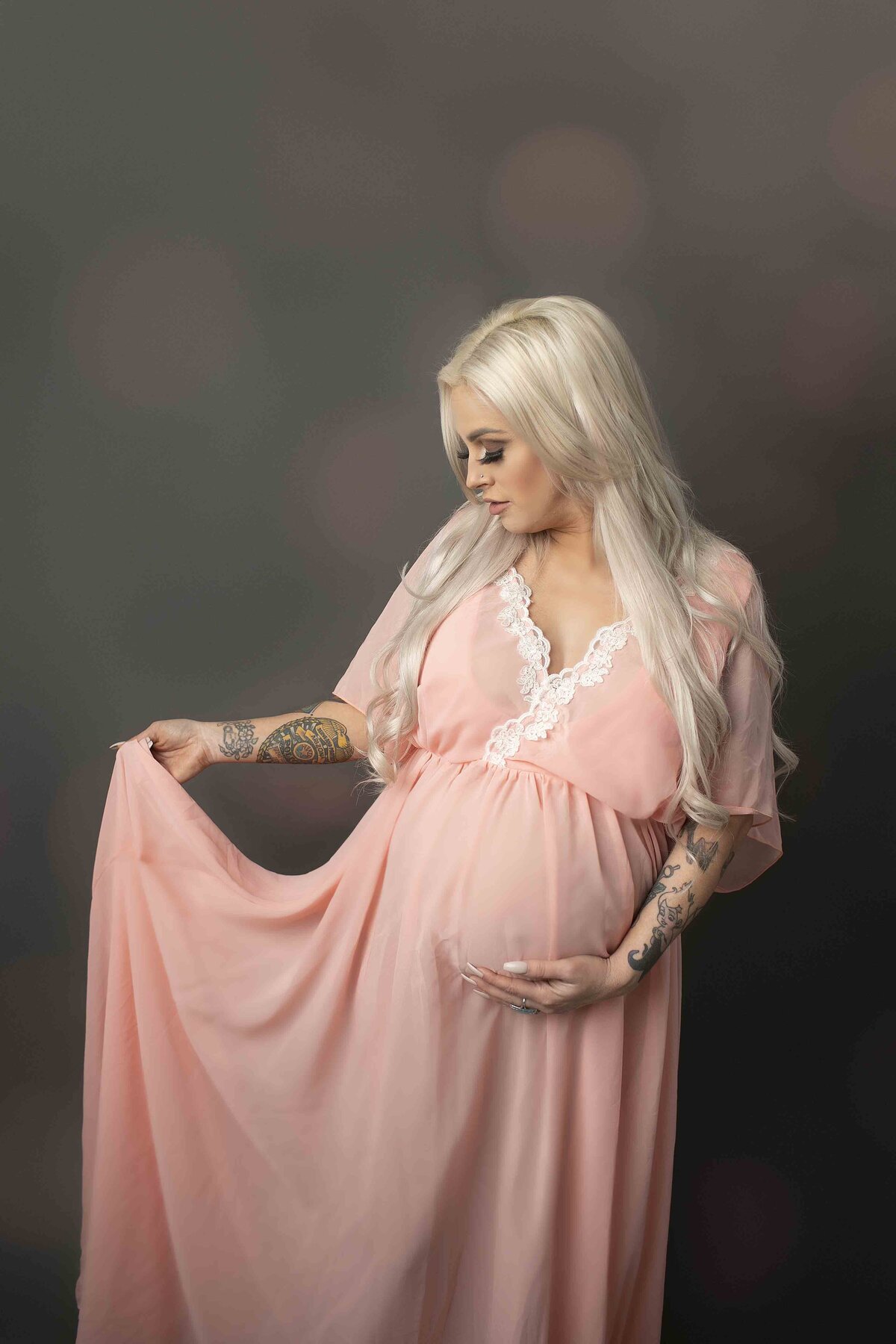 A striking studio maternity photo of the expectant mom, showcasing her tattoos while gently cradling her belly, dressed in a simple, elegant outfit that highlights her unique style, beautifully captured by Chunky Monkey Photography.